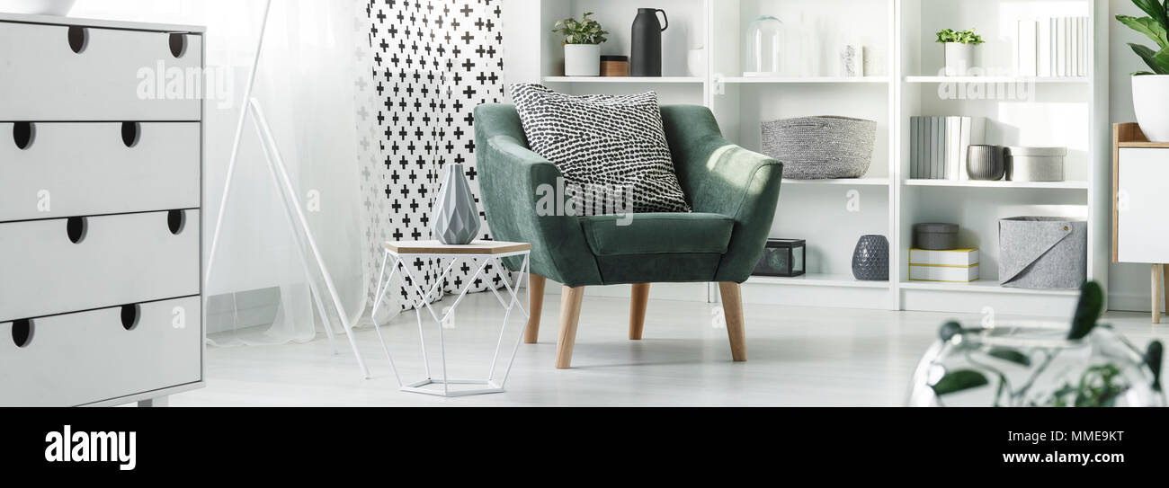 En bout de table en métal et en bois avec vase en céramique vert debout près d'un fauteuil avec coussin noir et blanc avec motif dans salon lumineux intérieur Banque D'Images