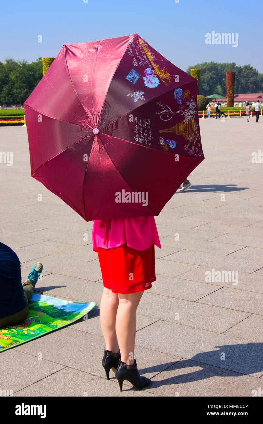 Une femme sur la place Tienanmen, à Beijing, Chine, tenant un parapluie décoré de symboles parisiens, comme la Tour Eiffel, et texte français. Banque D'Images