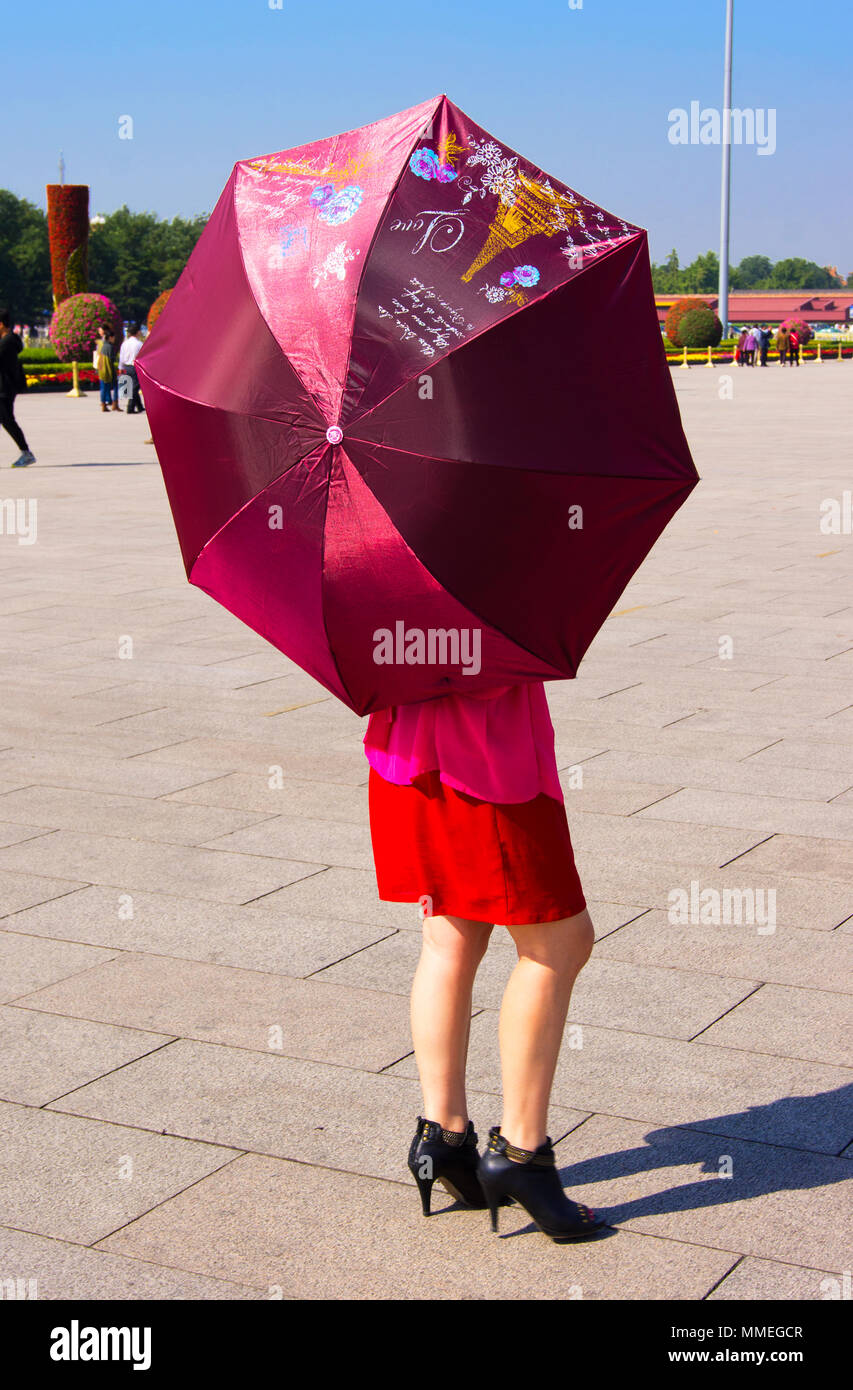 Une femme sur la place Tienanmen, à Beijing, Chine, tenant un parapluie décoré de symboles parisiens, comme la Tour Eiffel, et texte français. Banque D'Images