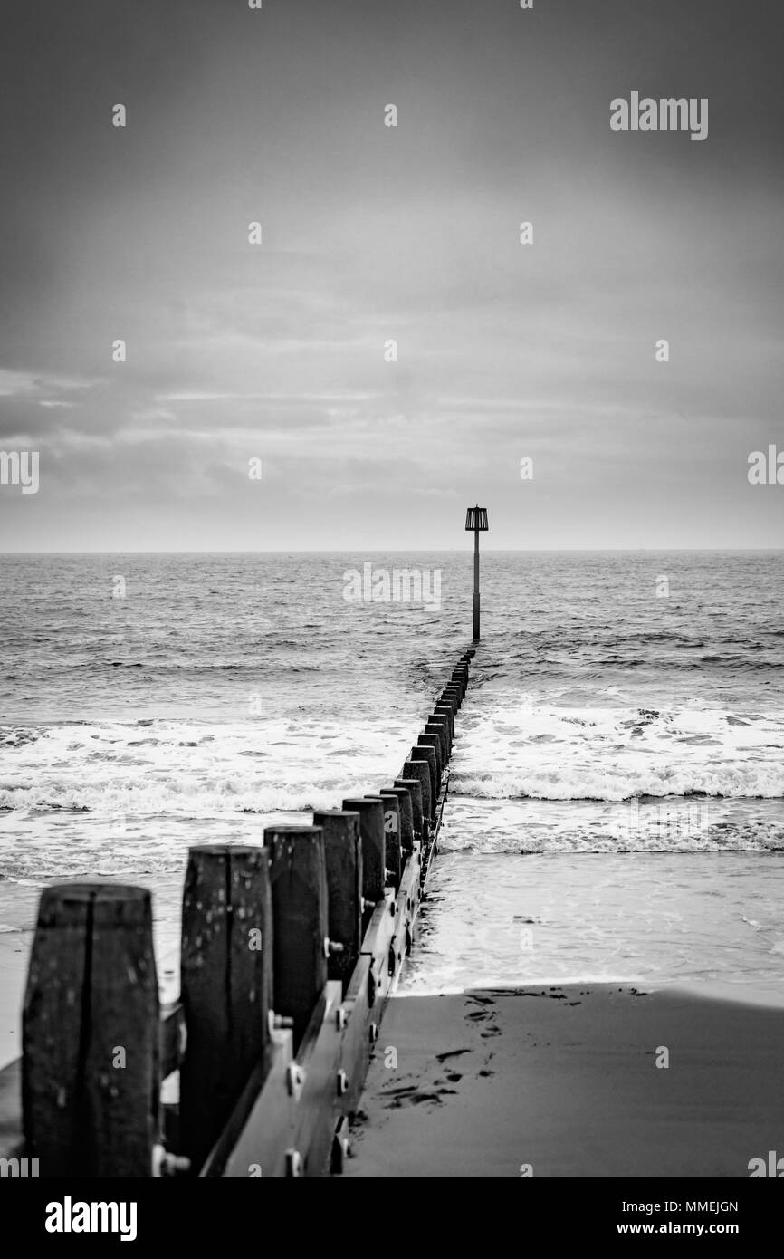 Vagues se briser contre une jetée qui s'étend sur la mer au large de la côte d'Exmouth. Tourné en noir et blanc pendant la saison d'hiver. Banque D'Images