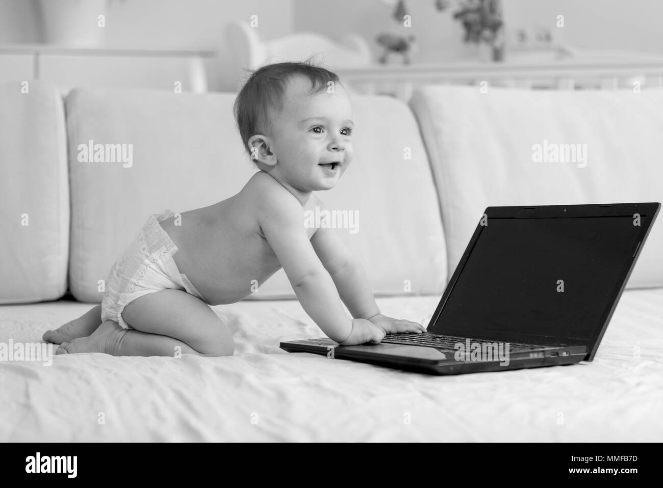Photo en noir et blanc de l'adorable smiling baby boy sitting on sofa and using laptop Banque D'Images