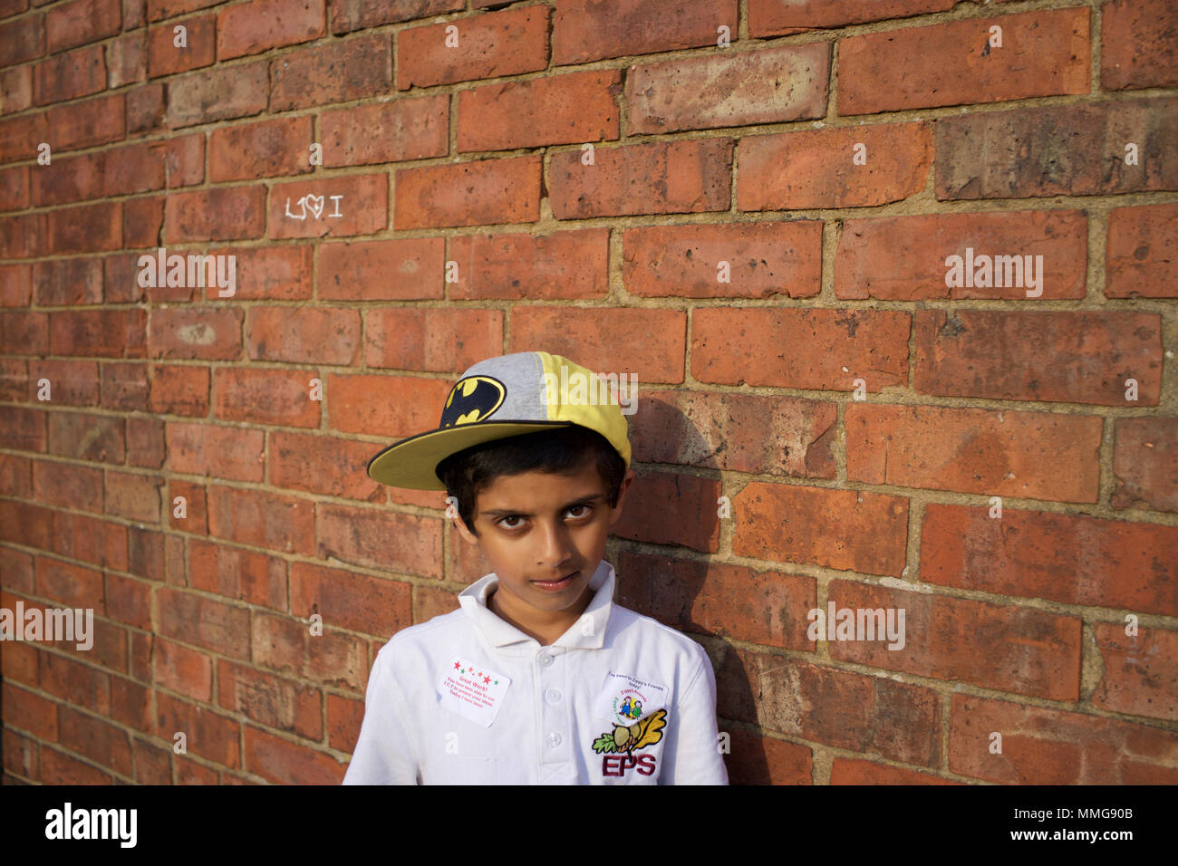 Garçon pakistanais à Batman Baseball Hat Standing par mur de briques, Rugby, Angleterre Banque D'Images