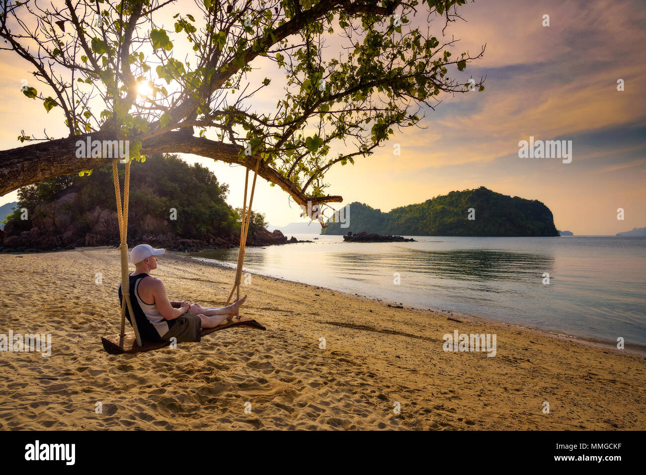 Jeune homme aime coucher de soleil sur une balançoire à une plage en Thaïlande Banque D'Images