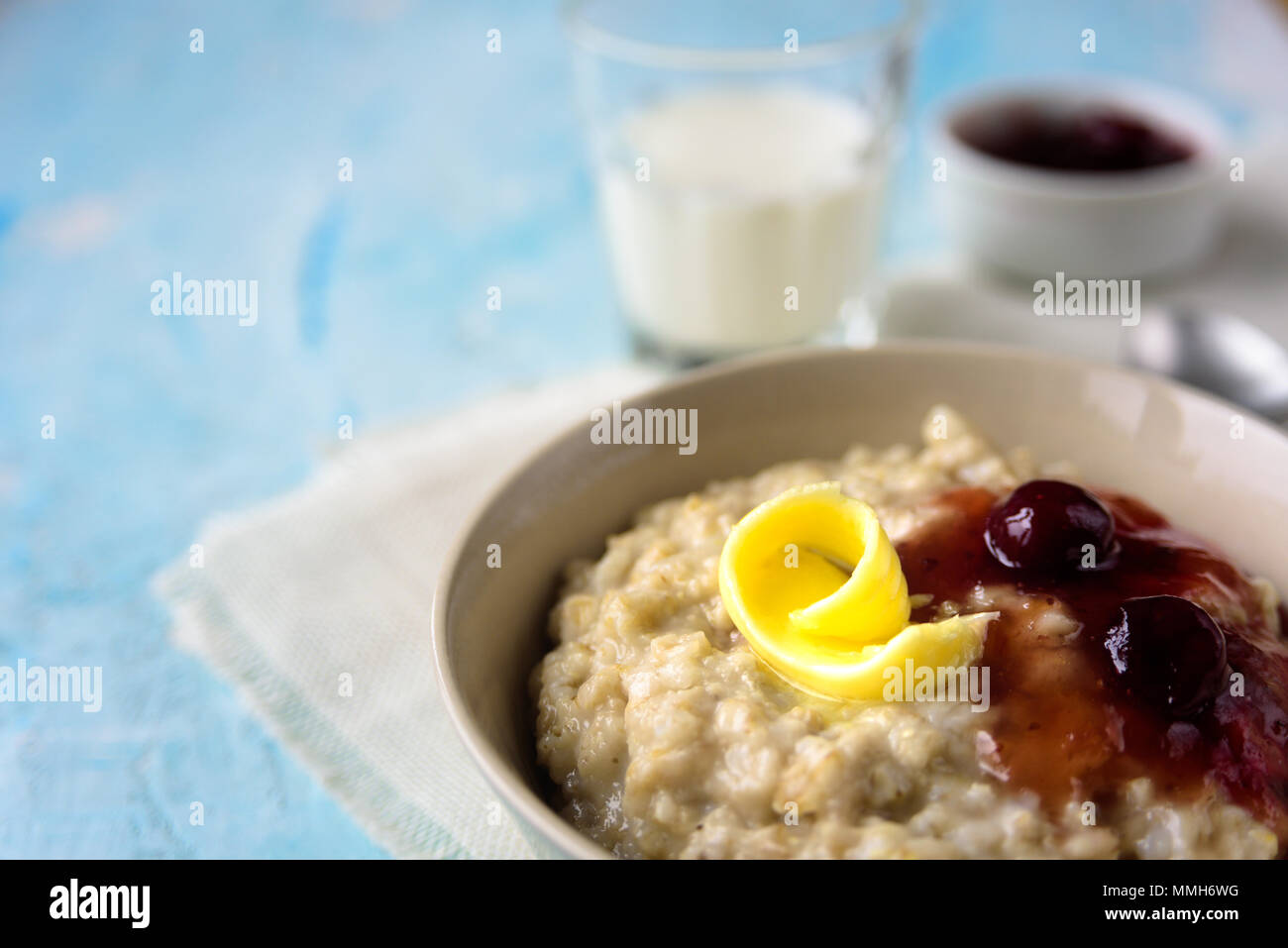 Gruau porrige avec beurre et confiture de cerise sur le tableau bleu. Avec le verre de lait. Le petit-déjeuner Banque D'Images