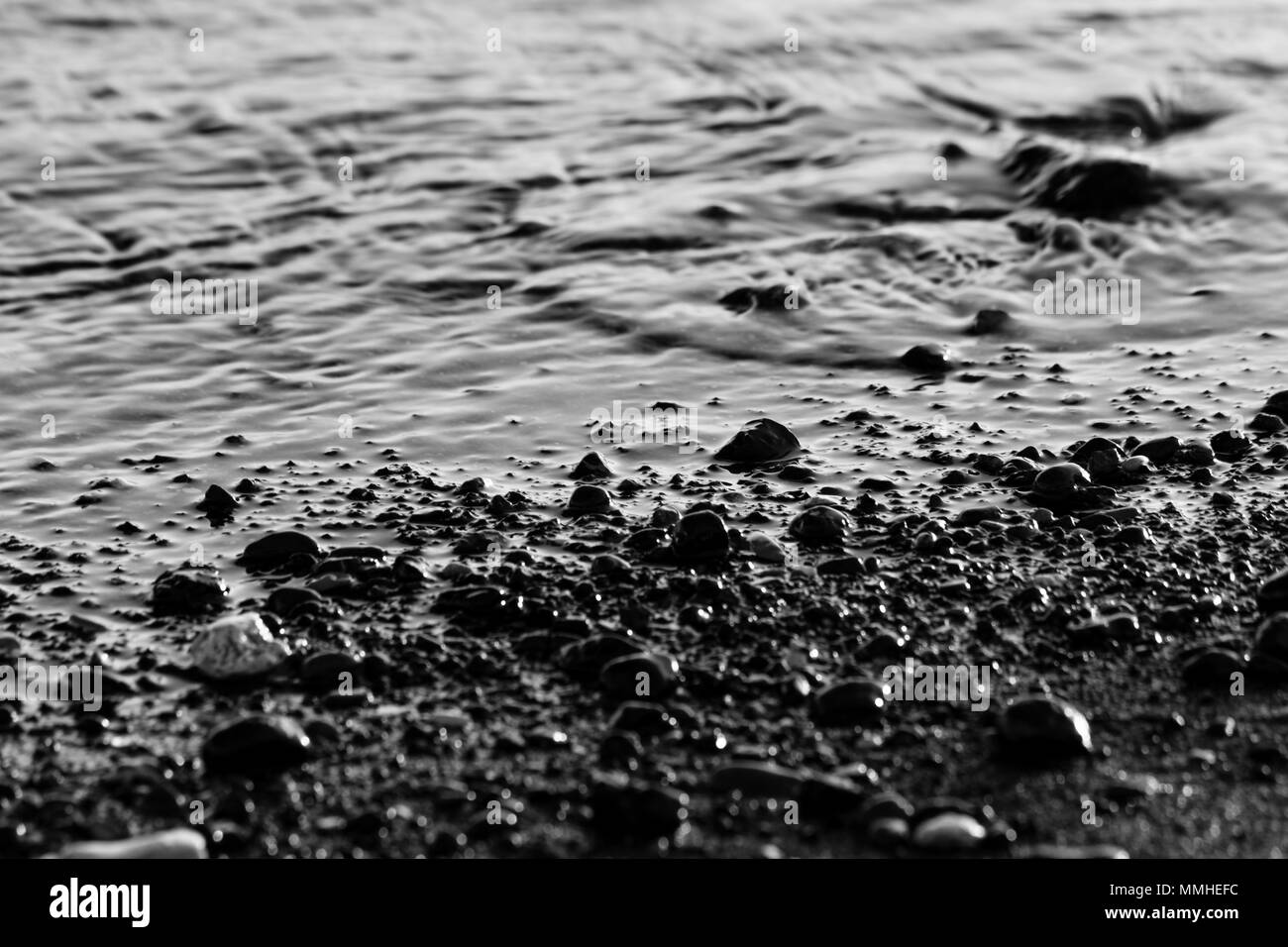 Une vue étroite de l'eau sur une rive du lac, avec les détails des sables et des petits cailloux ronds Banque D'Images