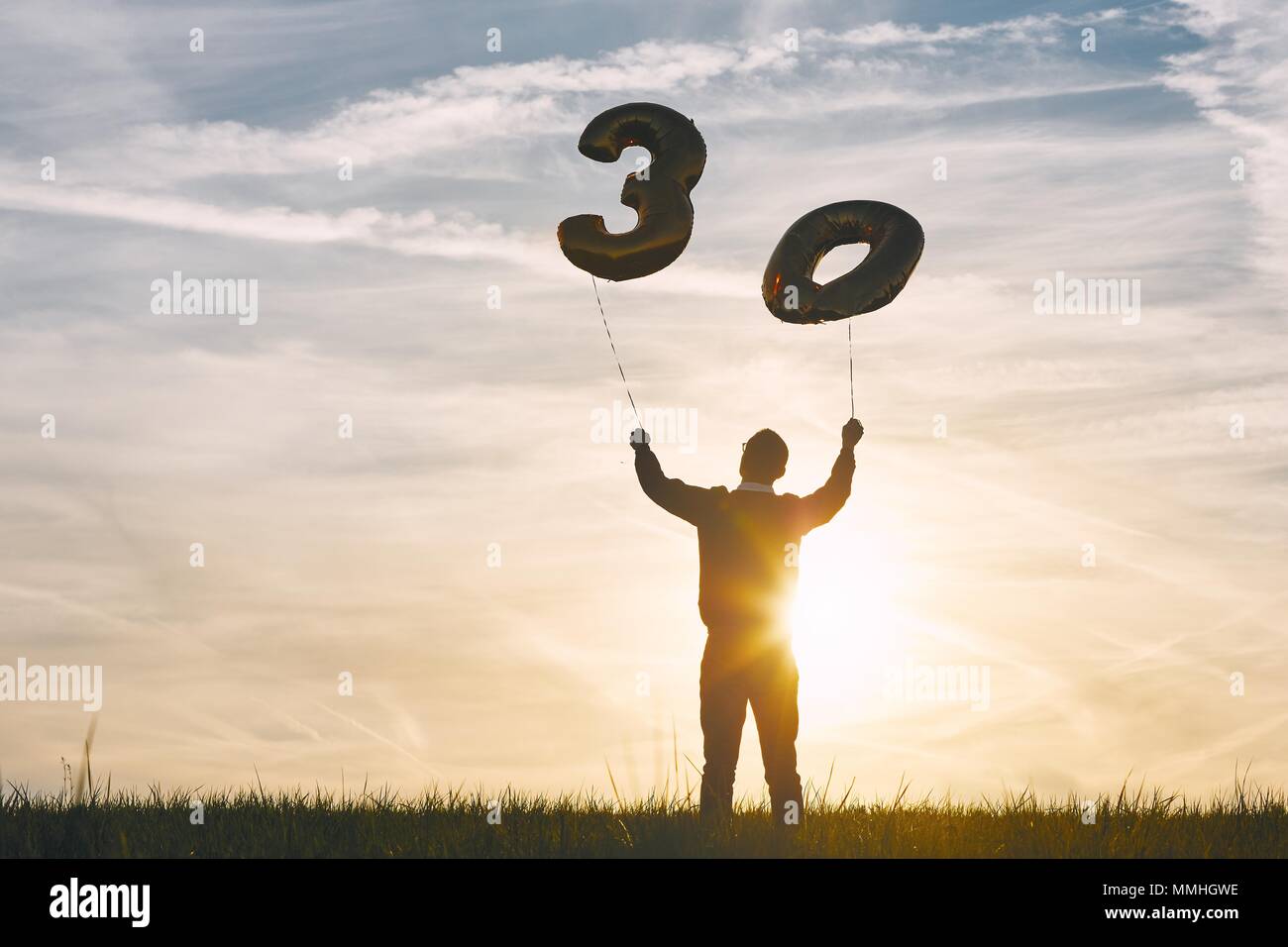 L'homme célèbre ses 30 années d'anniversaire. Personne tenant des ballons d'hélium en forme de numéro 30 au coucher du soleil. Banque D'Images