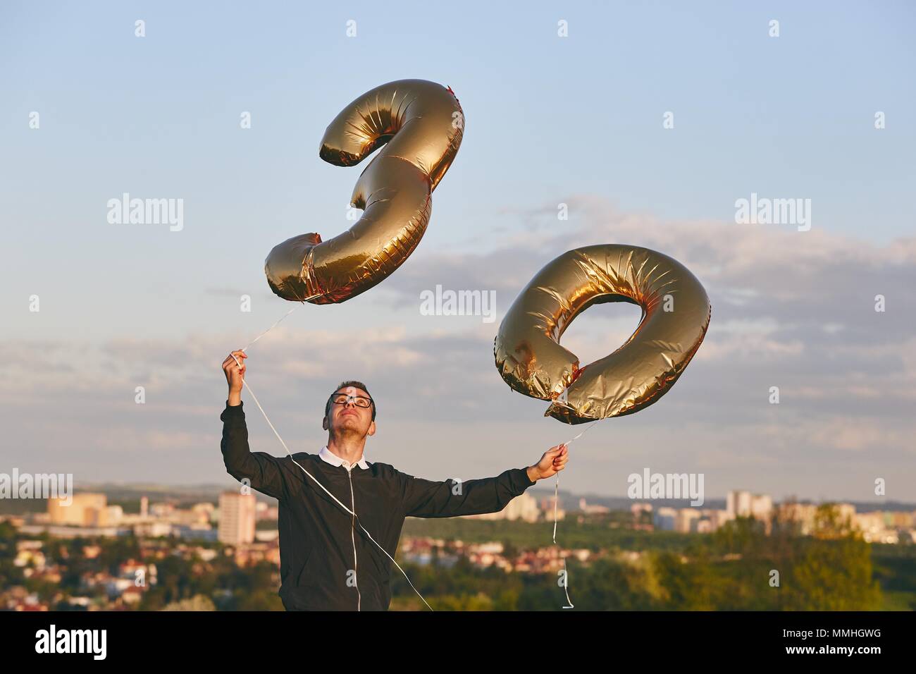 L'homme célèbre ses 30 années d'anniversaire. Personne tenant des ballons d'hélium en forme de numéro 30 contre city. Banque D'Images