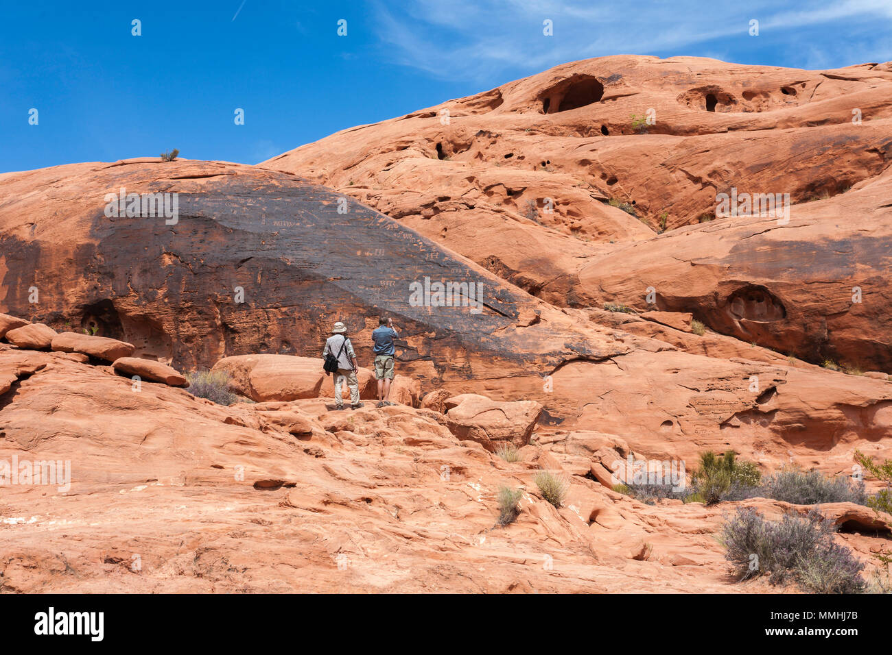 Les visiteurs photographient des symboles gravés dans des formations rocheuses de grès rouge dans le parc national de la Valley of Fire à Overton, Nevada, au nord-est de Las Vegas Banque D'Images