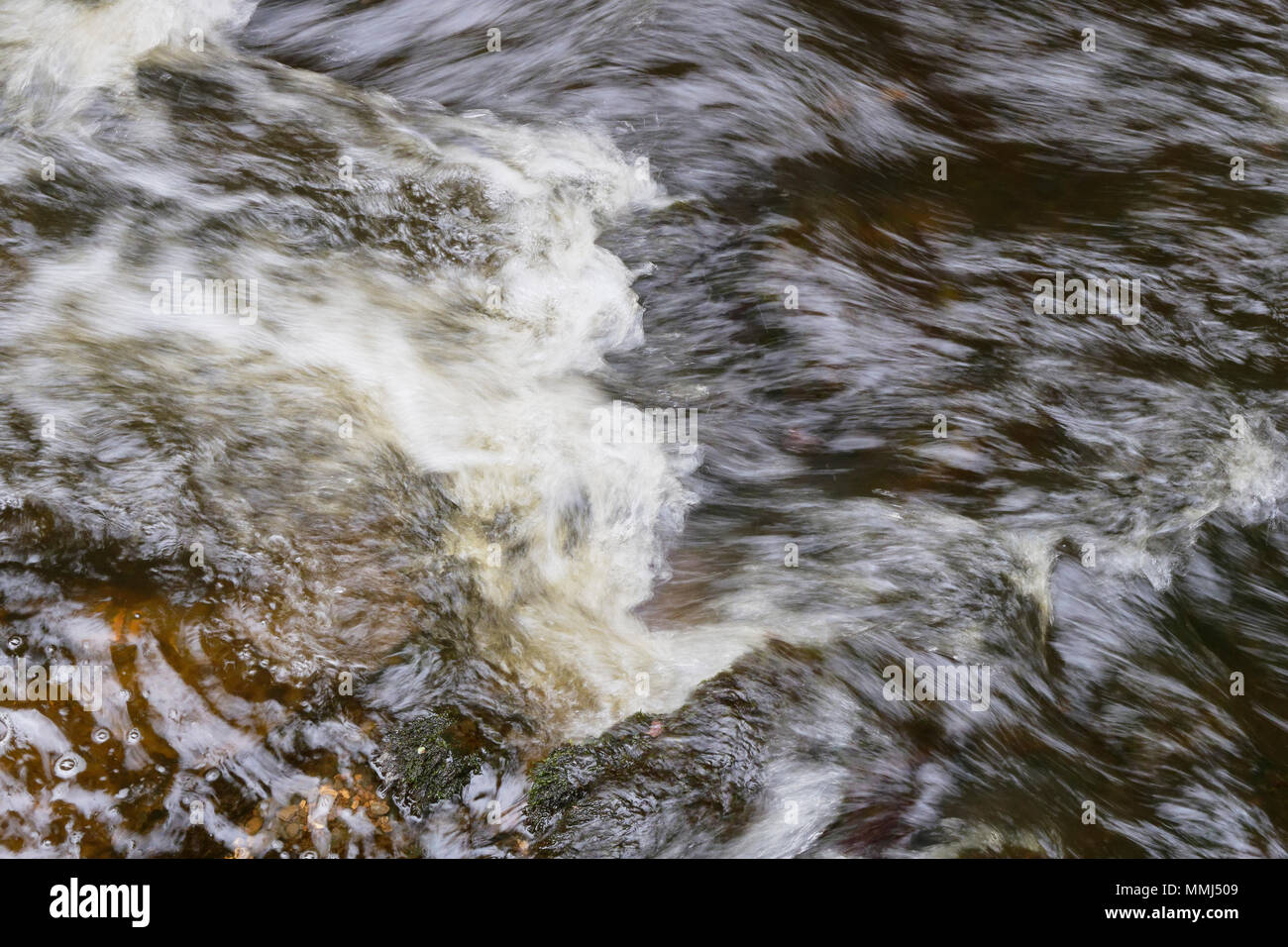 Close up de la surface d'un ruisseau qui coule sur des roches submergées tourbillonnantes. Banque D'Images