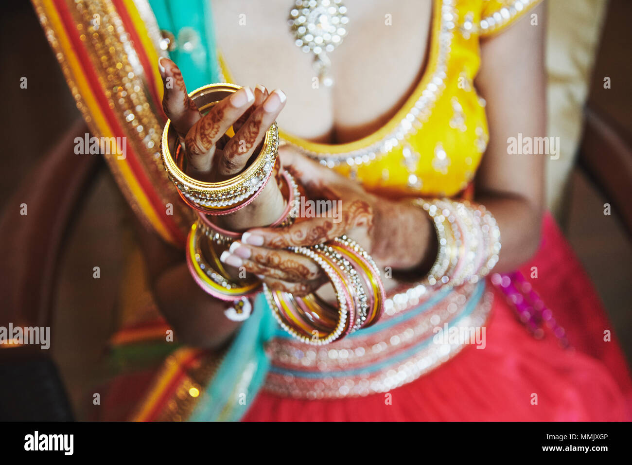 Le gros plan de la mariée indienne avec de beaux saree en blouse jaune et rouge en solde de mettre beaucoup de paillettes bracelets (bangle) sur la main avec mehnd Banque D'Images