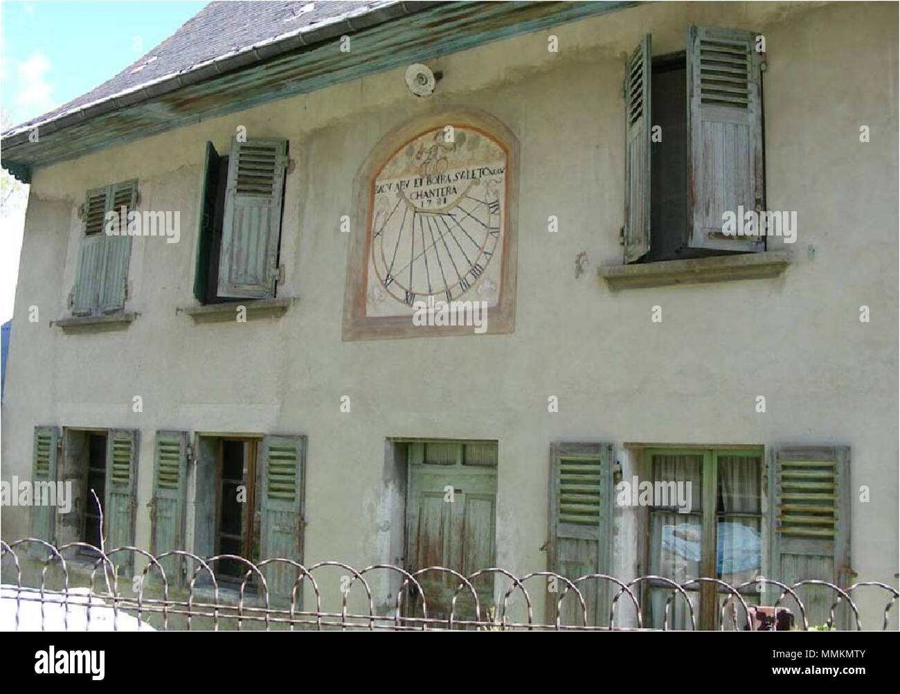 Cadran solaire sur la façade d'une vieille auberge. Décor : Deux nénuphars  Bacchus verre sur un baril d'une main une cruche et l'autre un gobelet. Il  porte une perruque et est