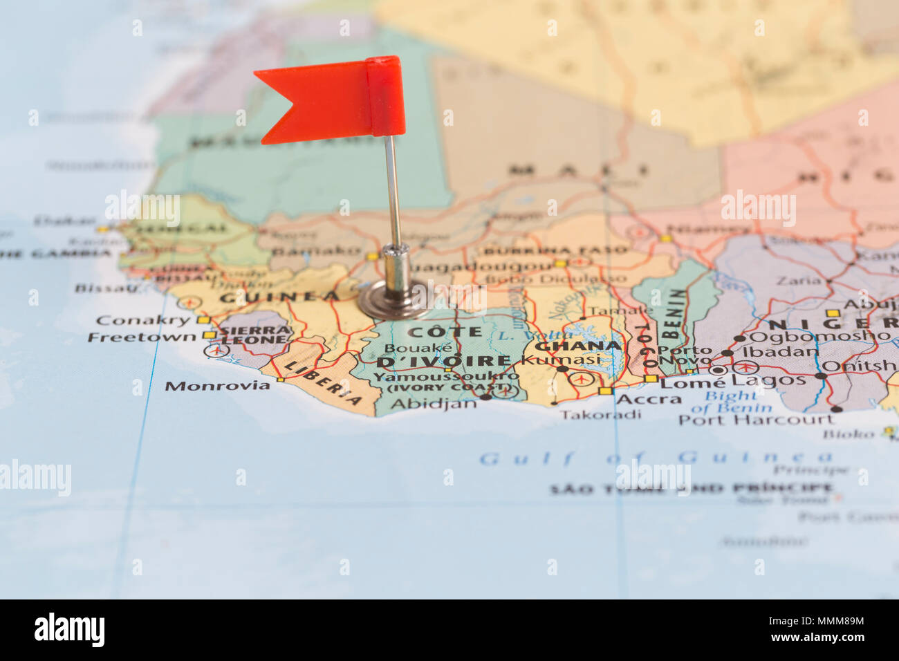 Petit drapeau rouge marquant le pays africain de la Côte d'Ivoire sur une carte du monde. Banque D'Images