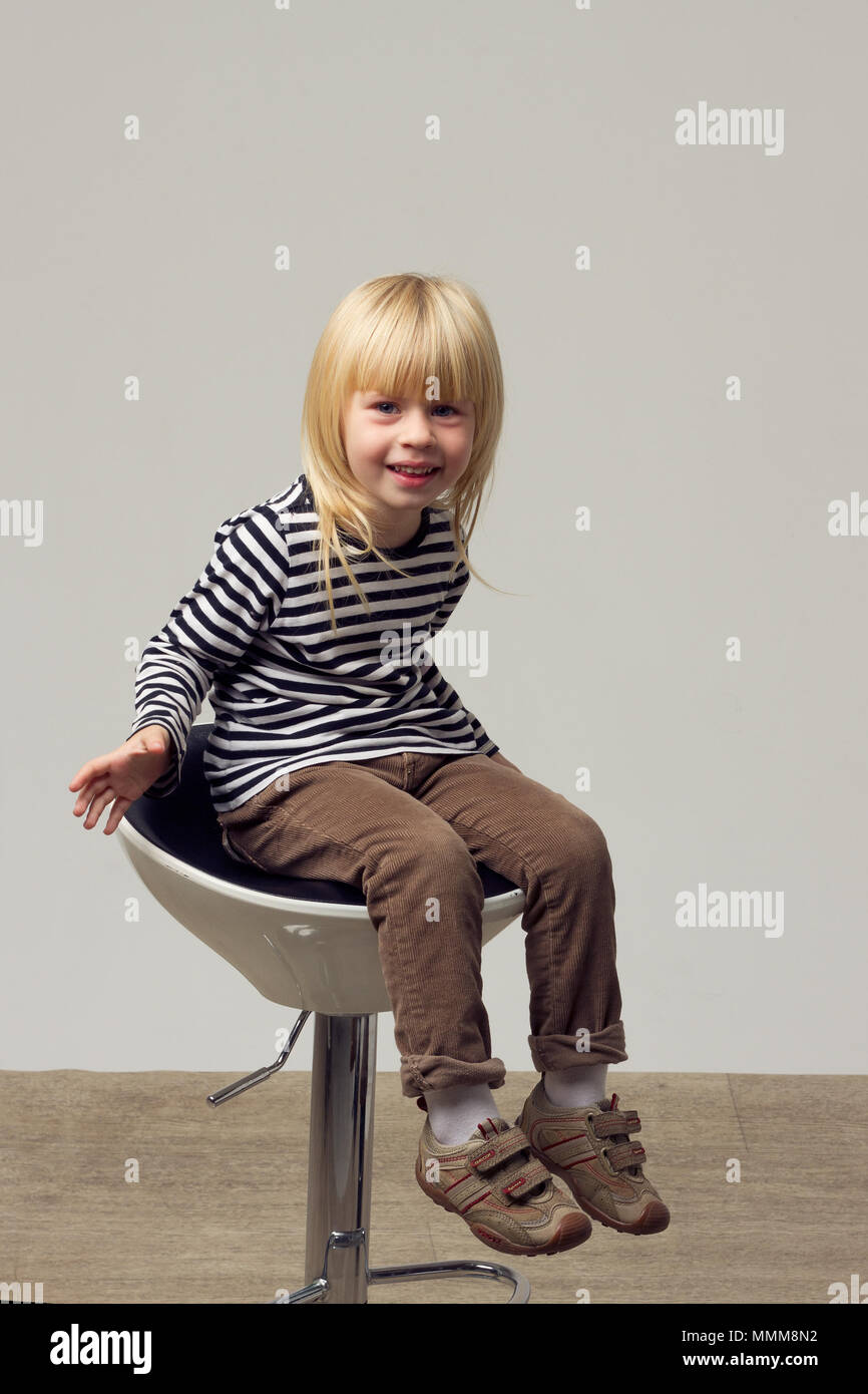 Fille blonde 3 ans en jeans est assis sur une chaise haute Banque D'Images