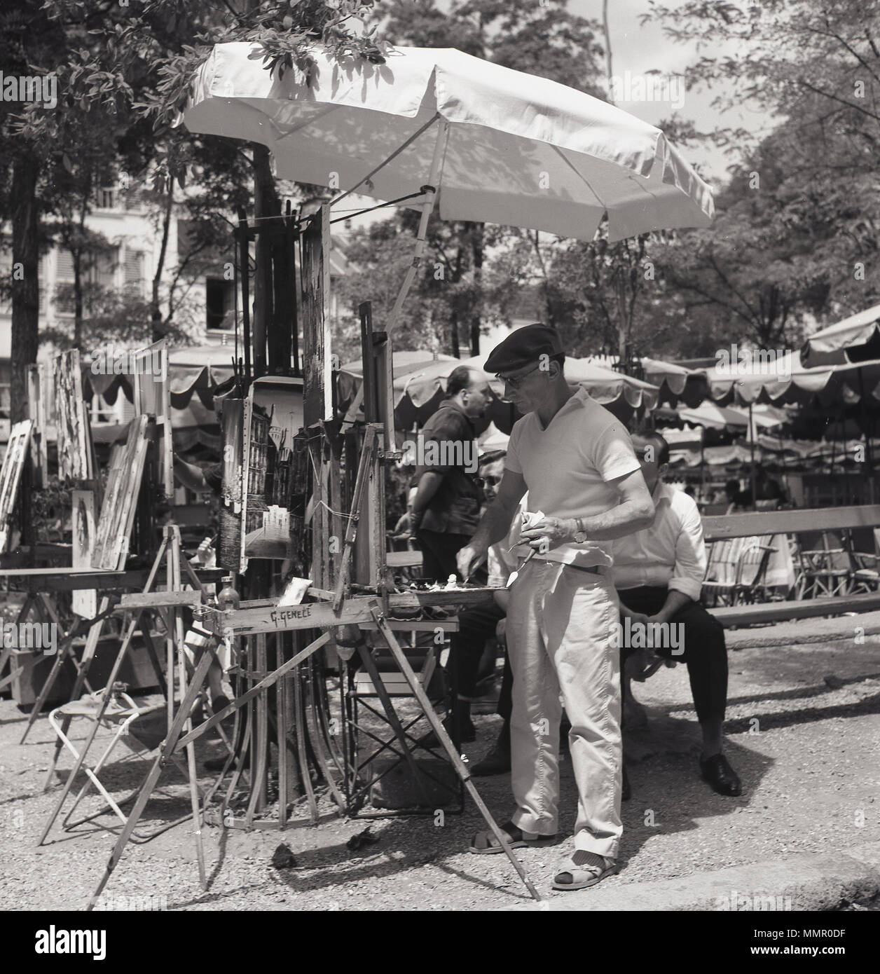 Années 1950, l'heure d'été à Paris et d'une artiste de rue sous un parapluie à l'œuvre à son chevalet à la place bordée d'arbres de la Place du Tertre à Montmartre. La place principale à Montmartre, dans le nord de la ville, est célèbre pour son patrimoine artistique et historique est une importante destination touristique à Paris. Banque D'Images