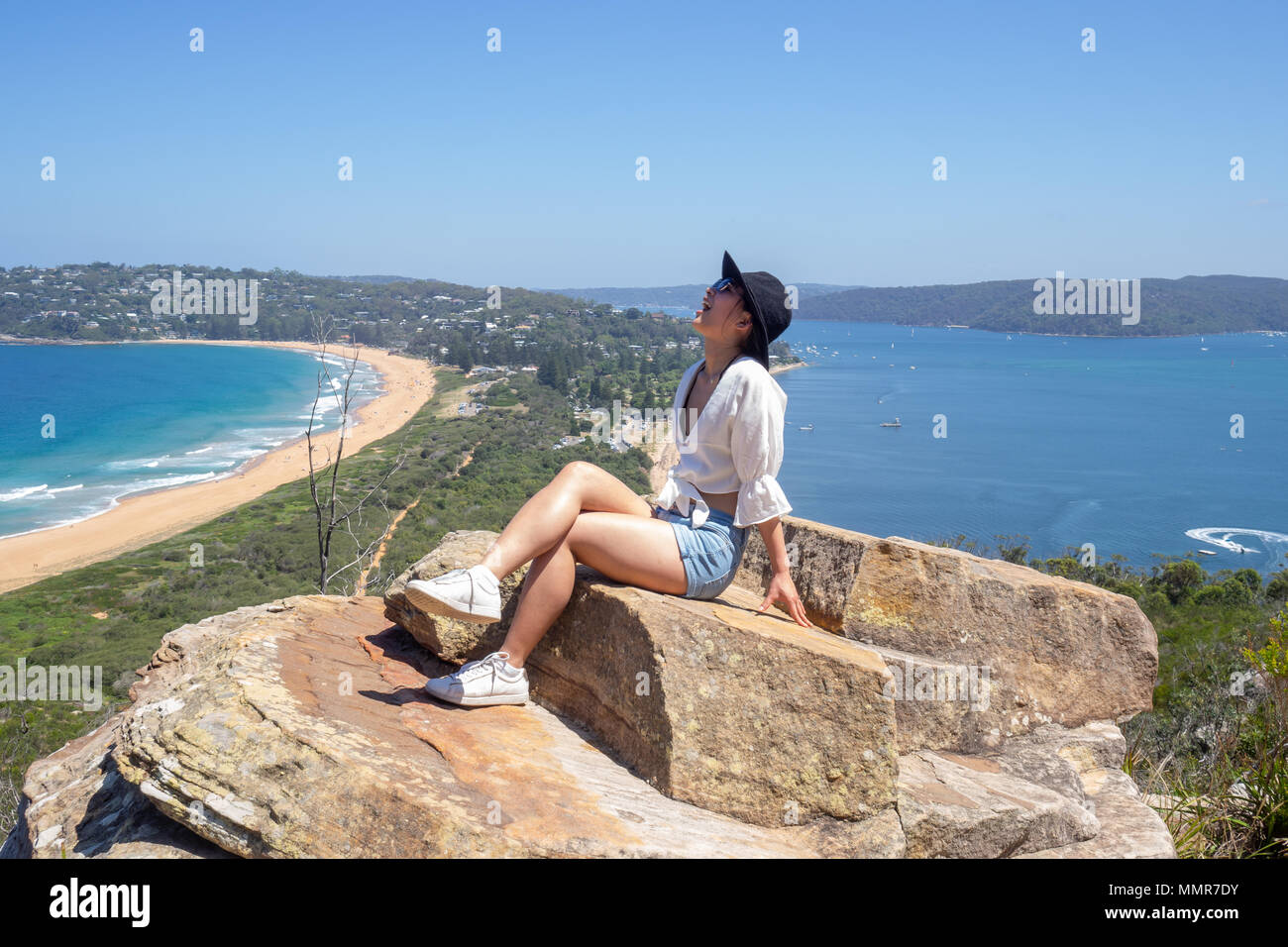 Jeune femme avec des lunettes se trouve sur l'arrière-plan de Palm Beach le haut d'un rocher au phare en Barrenjoey, Sydney, Australie. Banque D'Images