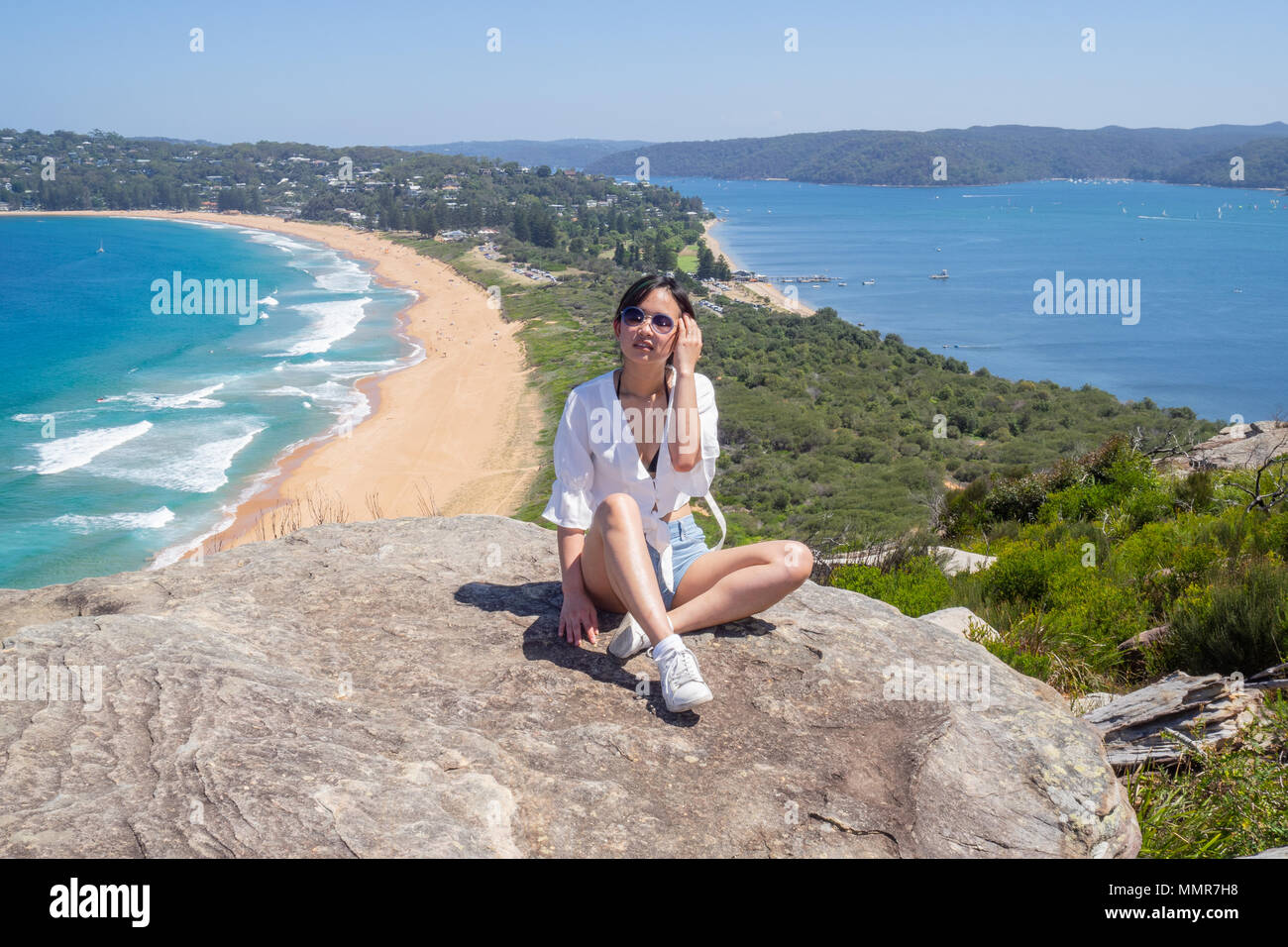 Jeune femme avec des lunettes se trouve sur l'arrière-plan de Palm Beach le haut d'un rocher au phare en Barrenjoey, Sydney, Australie. Banque D'Images