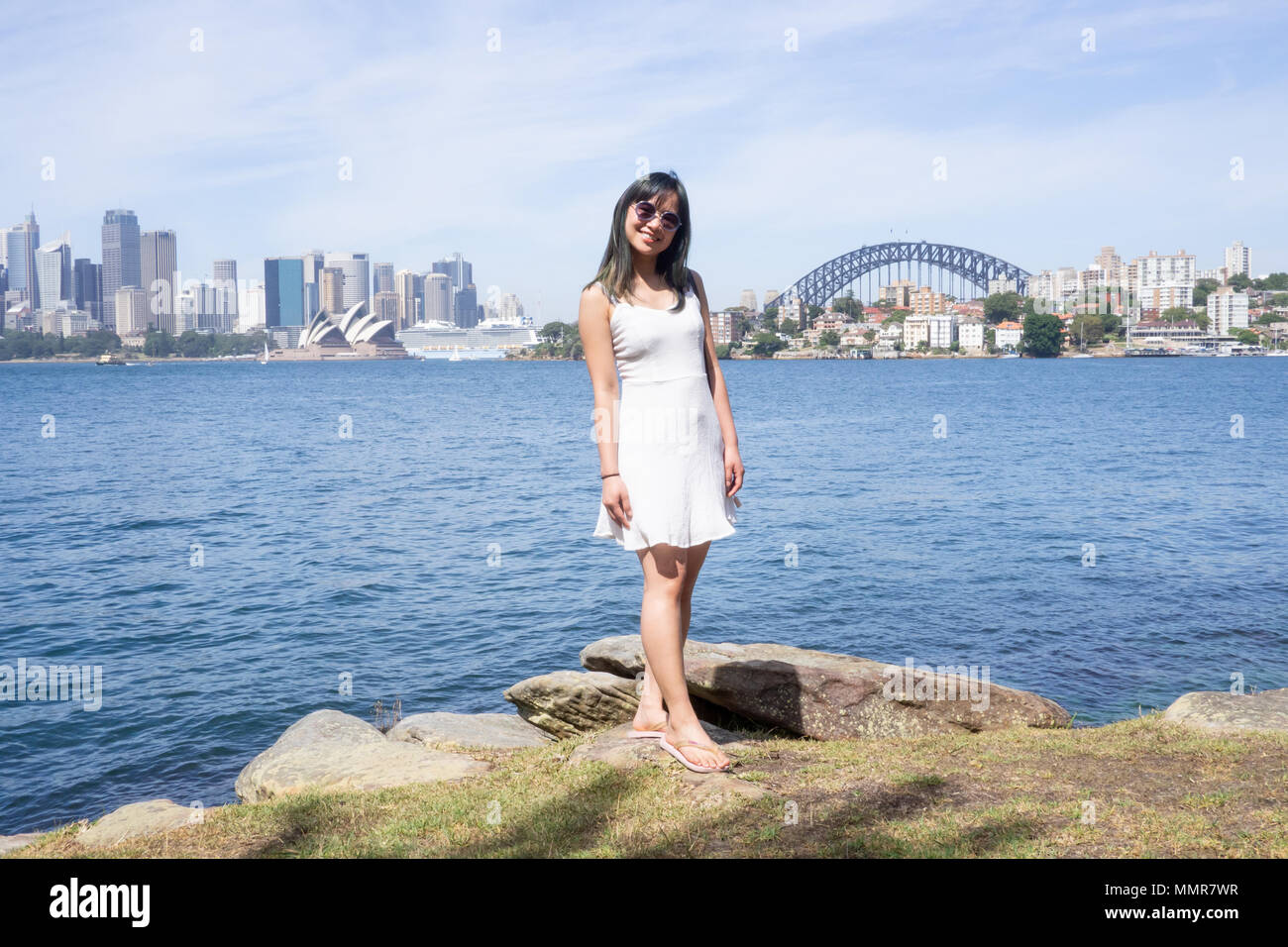 Jeune femme se tient sur l'arrière-plan de la belle ville de Sydney lors d'une journée ensoleillée dans une robe blanche et des lunettes Banque D'Images