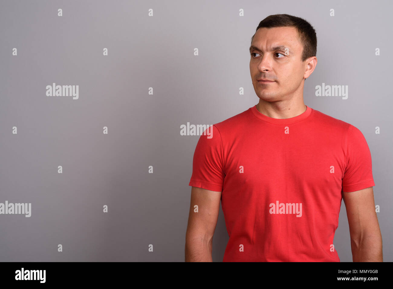 Homme portant un tee-shirt rouge à l'arrière-plan gris Banque D'Images