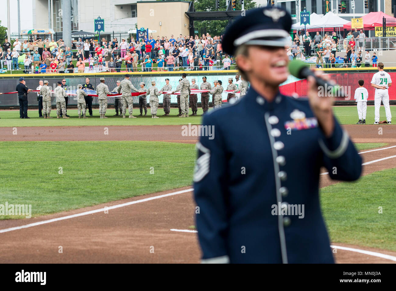 Le sergent-chef. Alyson Jones, Air Force Band de chanteur de vol, chante l'hymne national que les premiers intervenants d'urgence de Wright-Patterson Air Force Base, Ohio, tenir un drapeau géant en champ droit au cours de la Dayton Dragons hommage aux héros à Fifth Third Field au centre-ville de Dayton, le 5 août 2017. La foule a également observé que le colonel McDonald a administré le serment d'engagement personnel à l'enrôlement différé pendant le jeu. (U.S. Air Force photo/ Wesley Farnsworth) Banque D'Images