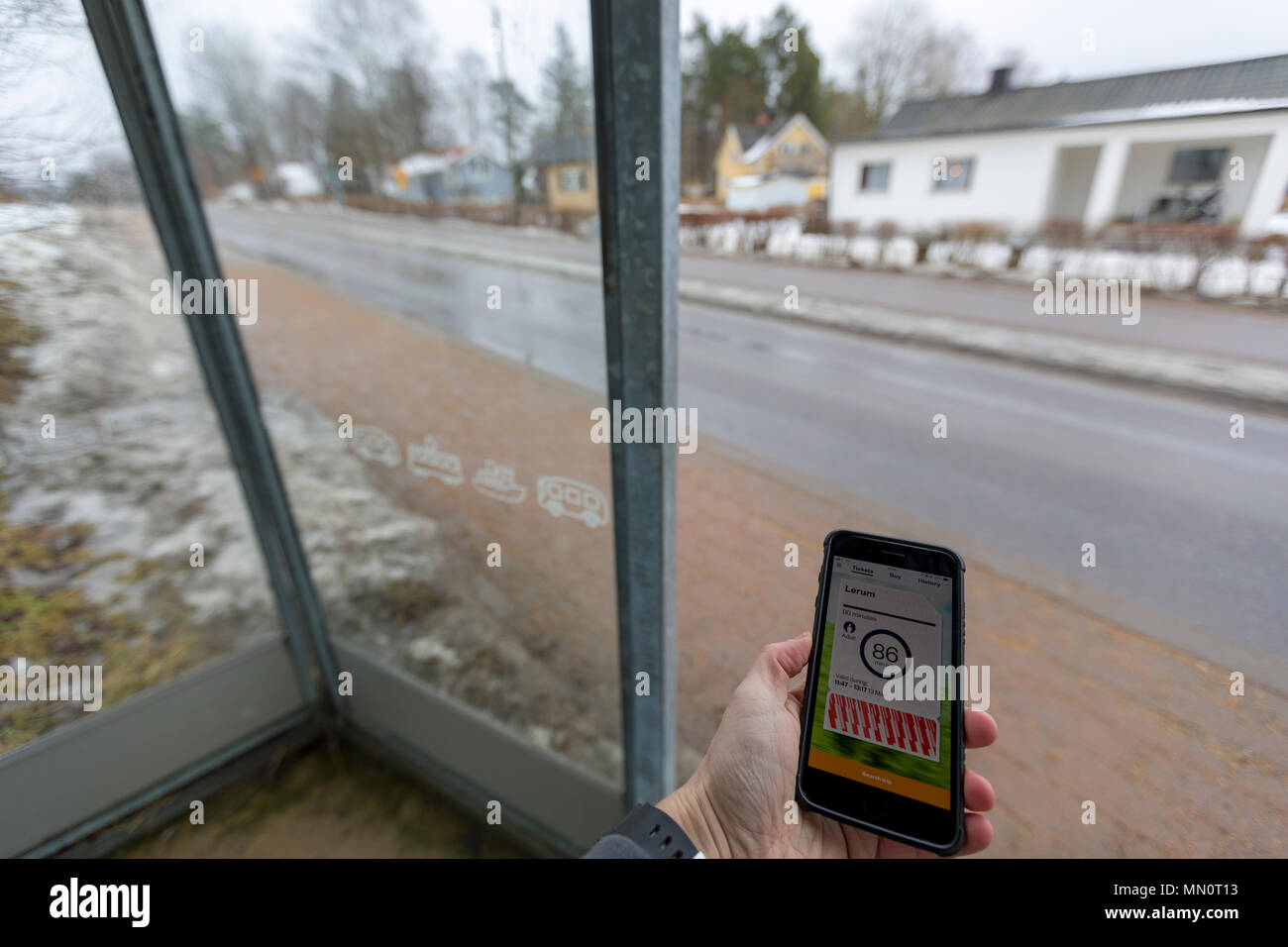 En attente de l'homme à la gare routière de bus tenant un smartphone iPhone téléphone mobile avec ticket de bus numérique valide sur l'affichage Banque D'Images