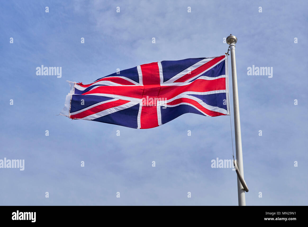 Union Jack flag fluttering dans une légère brise sur un mât contre un ciel bleu pâle Banque D'Images