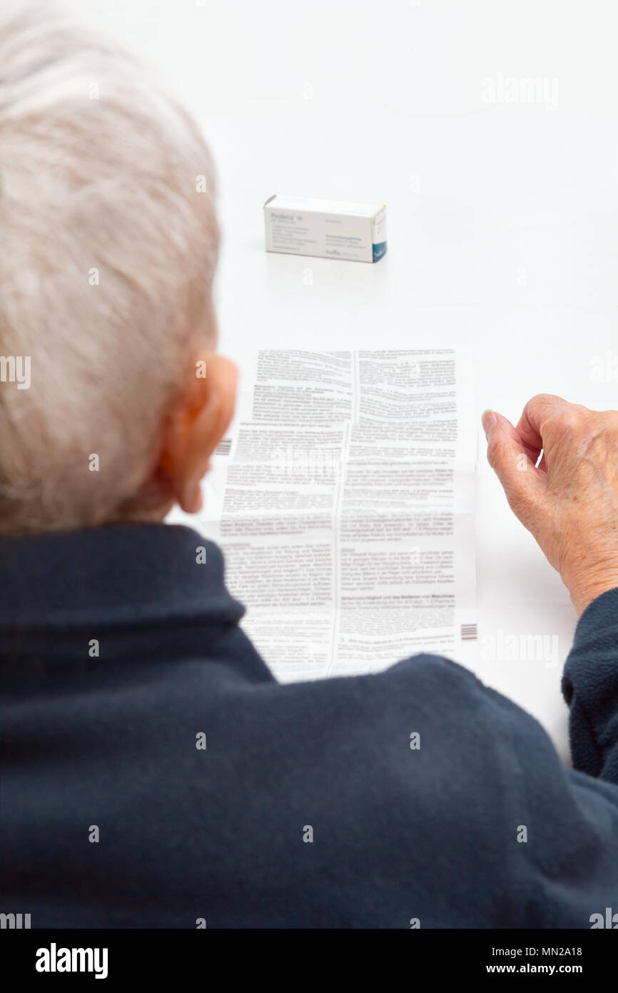 Vieille Femme assise à une table dans sa salle de séjour ne peut pas lire la feuille de renseignements de ses médicaments prescrits, car l'impression est trop petit Banque D'Images