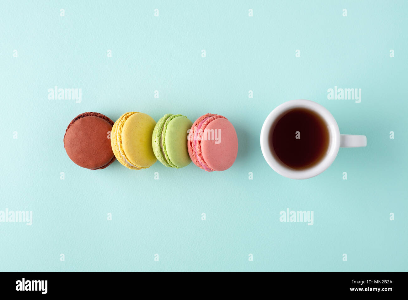 Une tasse de café avec quatre macarons colorés sur fond bleu turquoise. Style minimal de mise à plat avec place pour texte, vue d'en haut. Banque D'Images