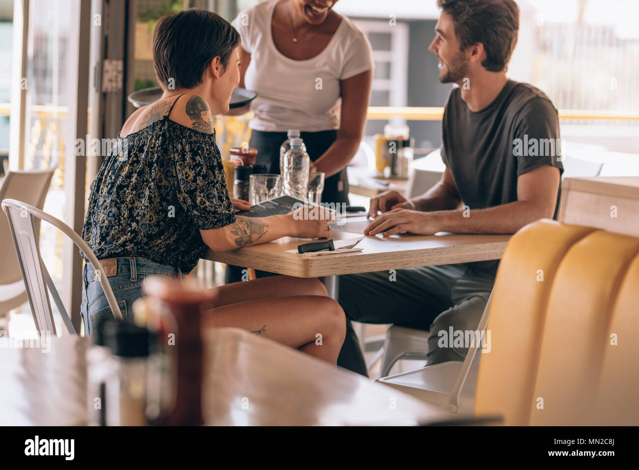 Jeune couple assis au café de donner ordre à un female waiter. L'homme de passer commande à une serveuse au restaurant alors qu'il était assis avec sa petite amie. Banque D'Images Jeune couple assis au café de donner ordre à un female waiter. L'homme de passer commande à une serveuse au restaurant alors qu'il était assis avec sa petite amie. Banque D'Images