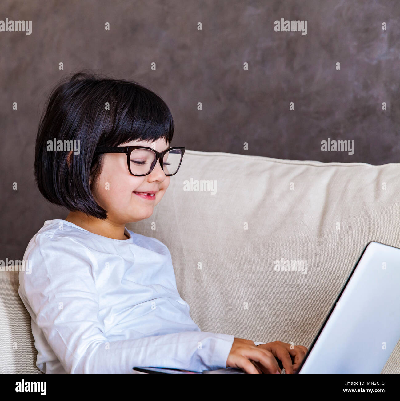 Jolie petite fille cheveux noir assis sur un canapé avec un ordinateur portable Banque D'Images