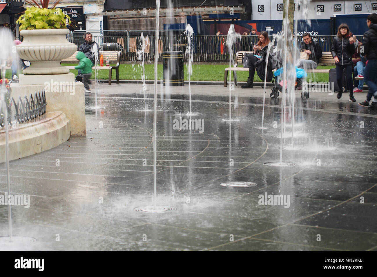 Des gens assis et debout dans Leicester Square, Londres, autour du dispositif de l'eau des fontaines Banque D'Images