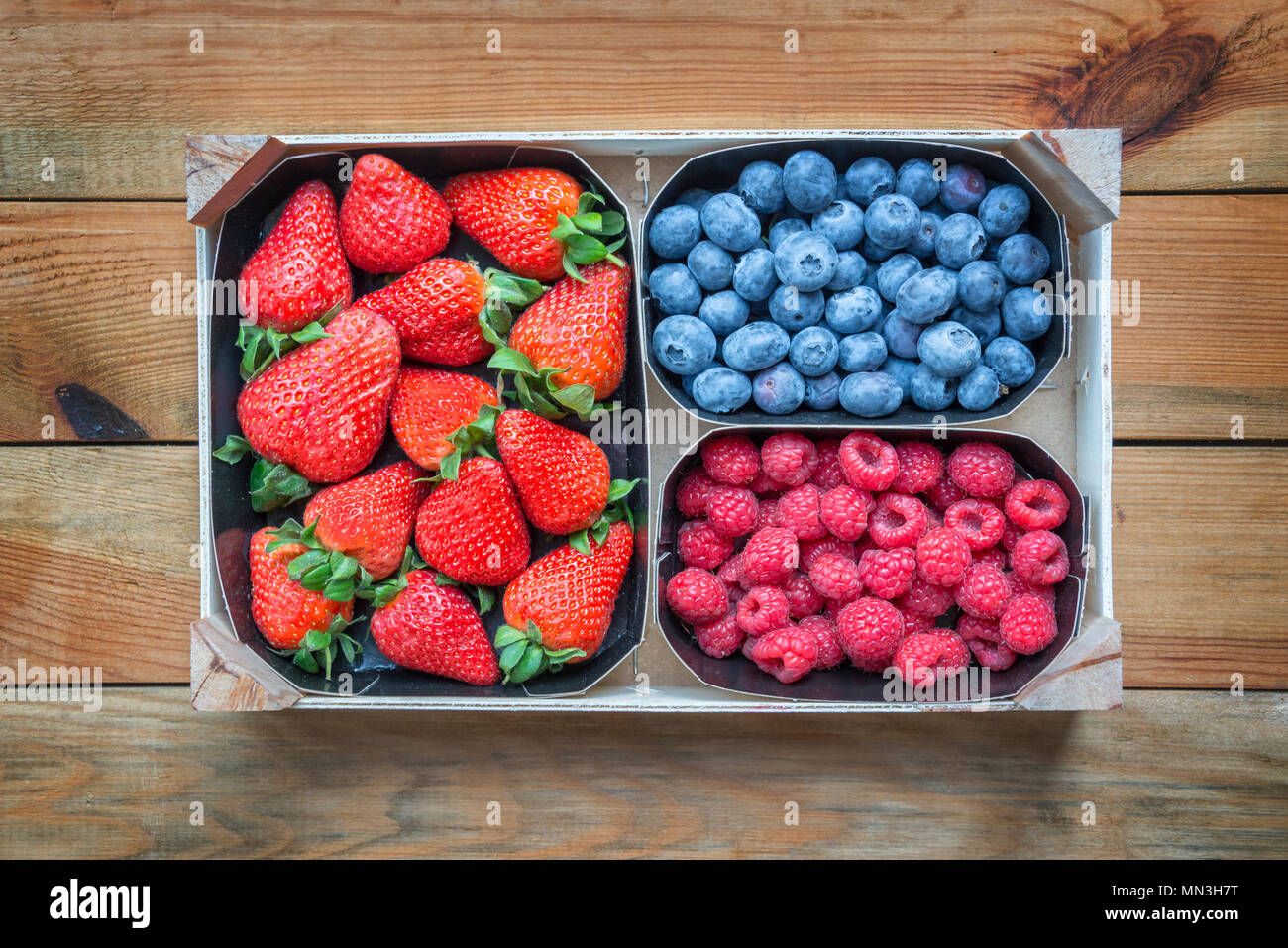 Mélange de fruits biologiques. Paniers de framboises, bleuets, fraises sur table en bois, vue du dessus Banque D'Images