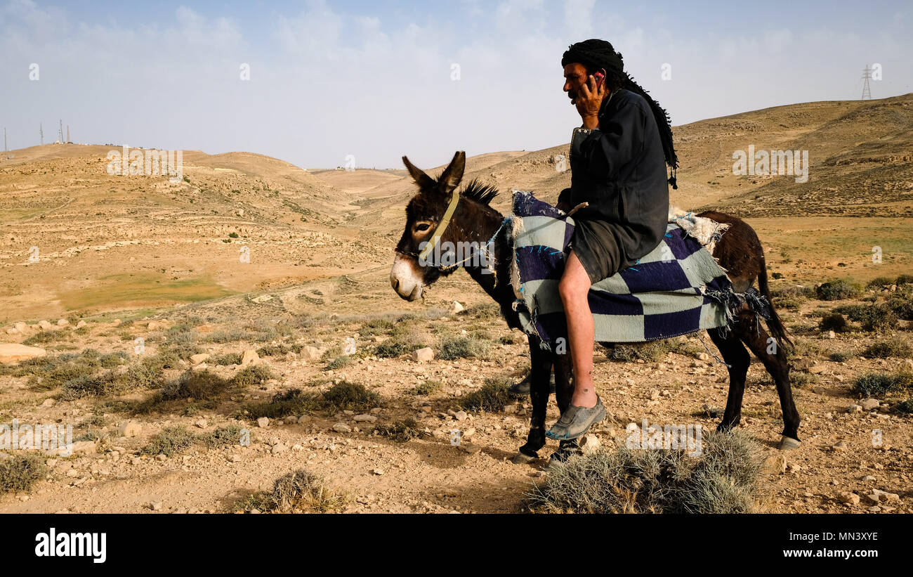 Un bédouin est appeler avec un téléphone cellulaire alors que sur son âne dans un paysage désertique Banque D'Images