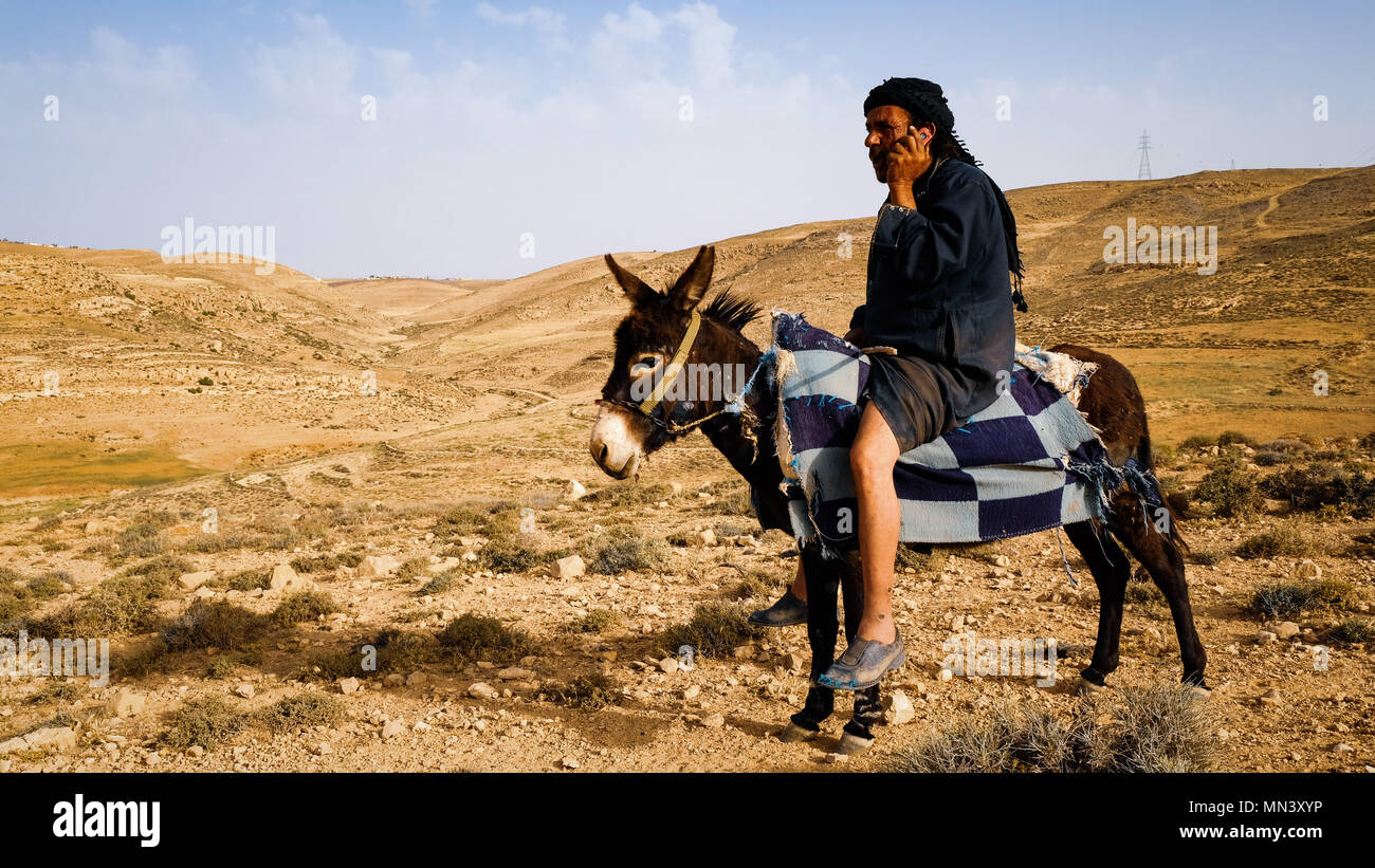 Un bédouin est appeler avec un téléphone cellulaire alors que sur son âne dans un paysage désertique Banque D'Images