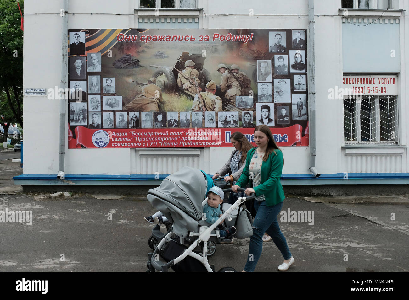 Des femmes poussant des poussettes passent devant une affiche avec de vieilles photographies de Russes qui ont combattu pendant la seconde Guerre mondiale dans le centre de Tiraspol, la capitale de Pridnestrovie, officiellement connue sous le nom de République moldave Pridnestrovienne PMR et également appelée Transnistrie depuis 1992 un État sécessionniste enclavé internationalement reconnu comme faisant partie de la Moldavie Banque D'Images