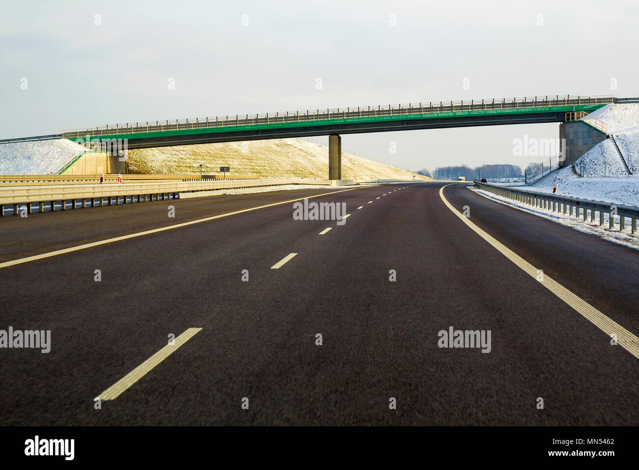 L'ensemble moderne d'asphalte lisse vide qui s'étend de l'autoroute à horizon sous haut pont tournant à droite passé forêt lointaine à jour. Voyage confortable, vitesse Banque D'Images