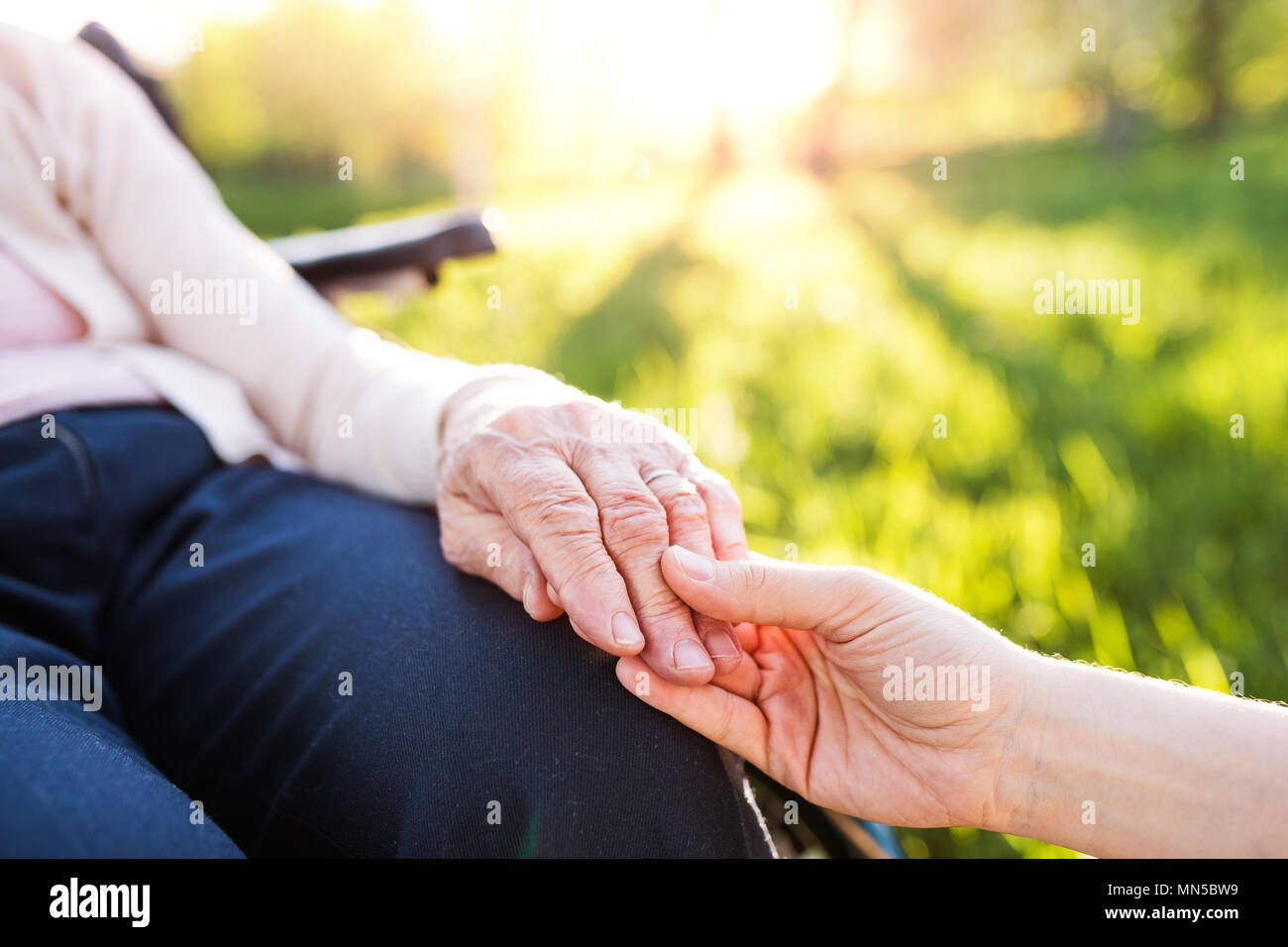 Petite-fille méconnaissable holding hand d'une vieille grand-mère en fauteuil roulant dans la nature au printemps. Banque D'Images