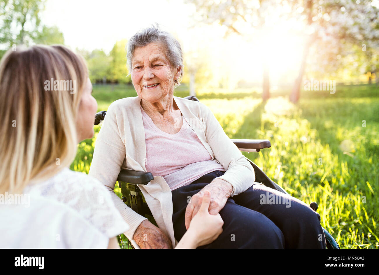 Une vieille grand-mère en fauteuil roulant avec une petite-fille adultes au printemps à l'extérieur de la nature, se tenant la main. Banque D'Images