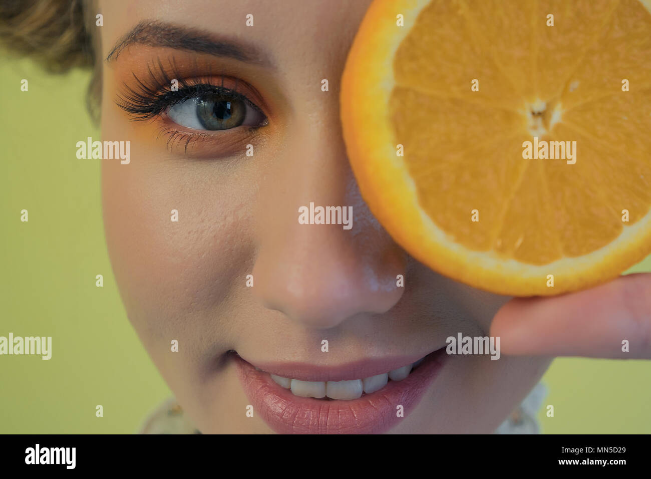 Une jeune fille drôle avec un professionnel de maquillage lumineux lui couvre les yeux avec de l'orange. La photographie de portrait Banque D'Images