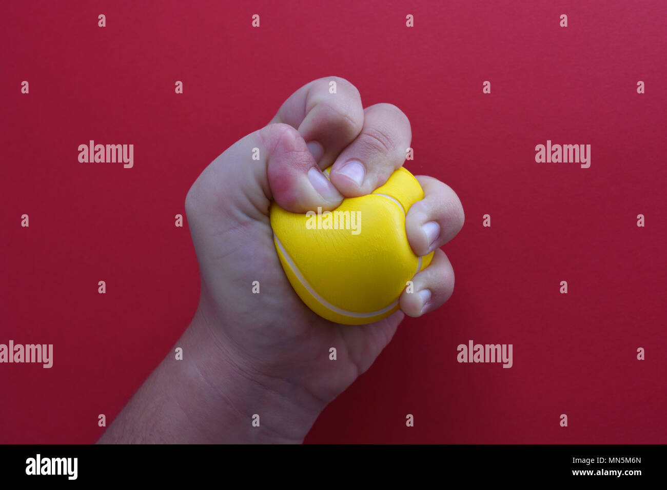 Woman squeezing une balle anti-stress, close-up, sur un fond rouge avec l'exemplaire de l'espace. Banque D'Images
