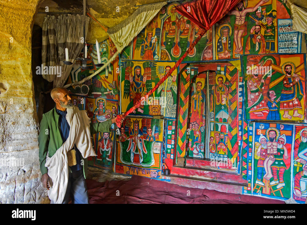 Prêtre montre peintures sur toile avec les thèmes bibliques dans l'interieur de l'église rupestres Mikael, Mellehayzengi Tsaeda Amba, Tigray, Éthiopie Banque D'Images