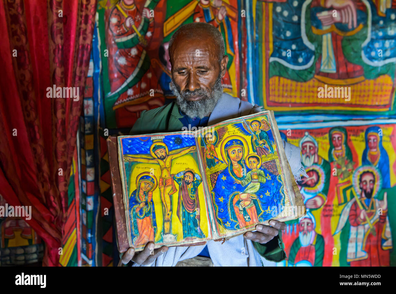 Prêtre de l'église rupestres Mikael Mellehayzengi montrant le livre des miracles de Maria avec des dessins peints à la main sur parchemin,Ethiopie Banque D'Images