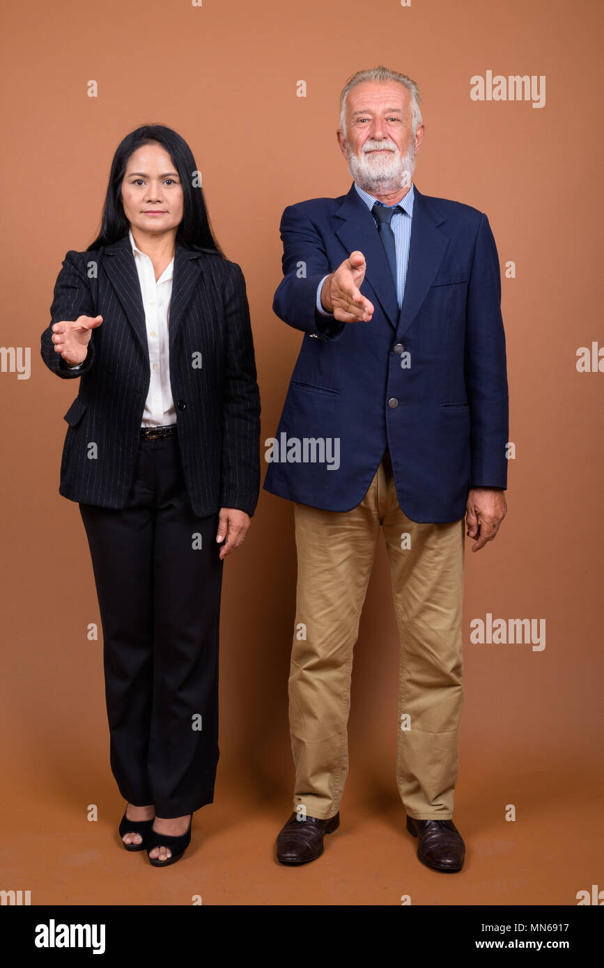 Multi-ethnique mature business couple contre fond brun Banque D'Images
