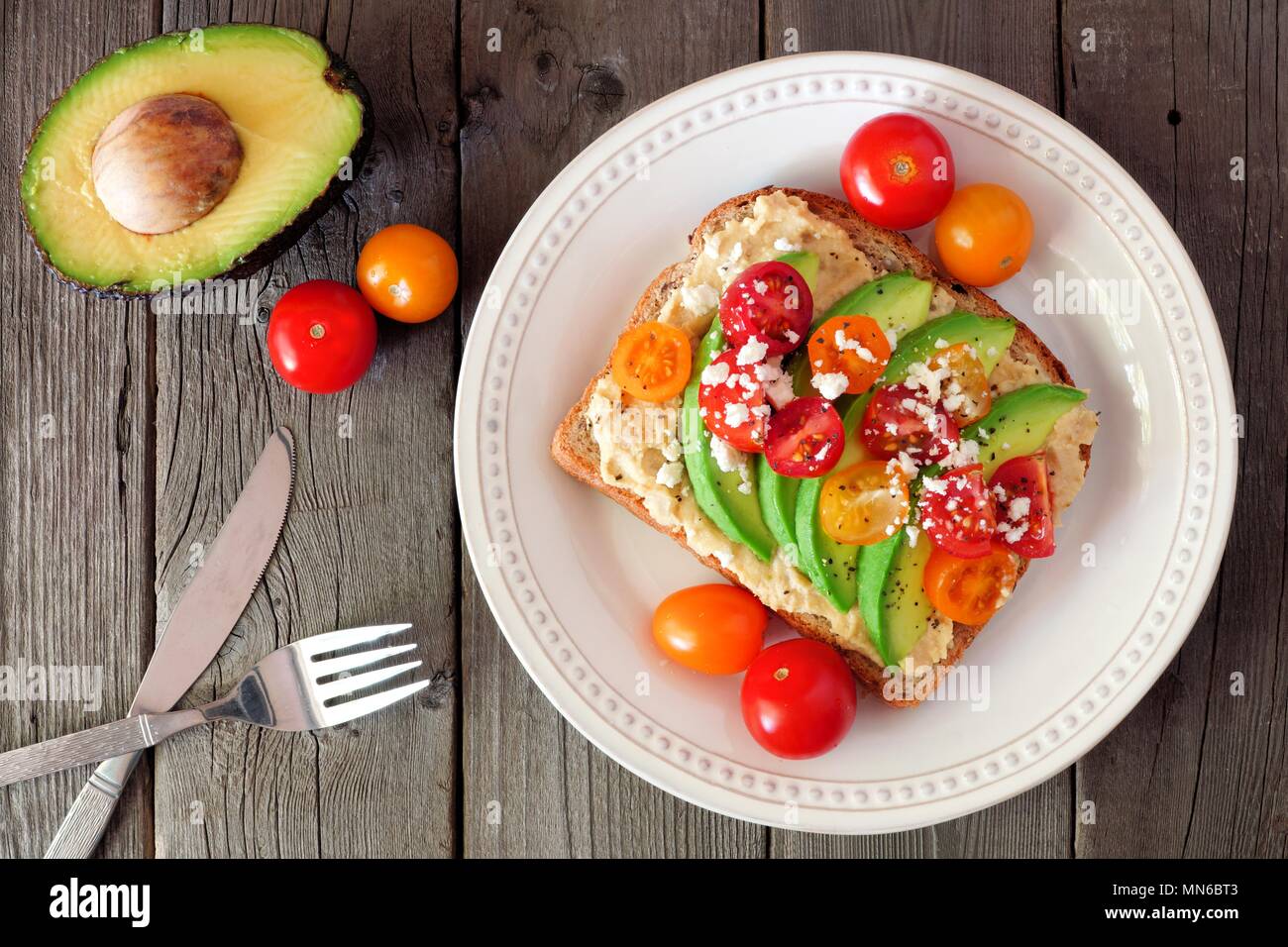 Toast à l'avocat d'hummus et les tomates sur la plaque, au-dessus de scène sur fond sombre Banque D'Images