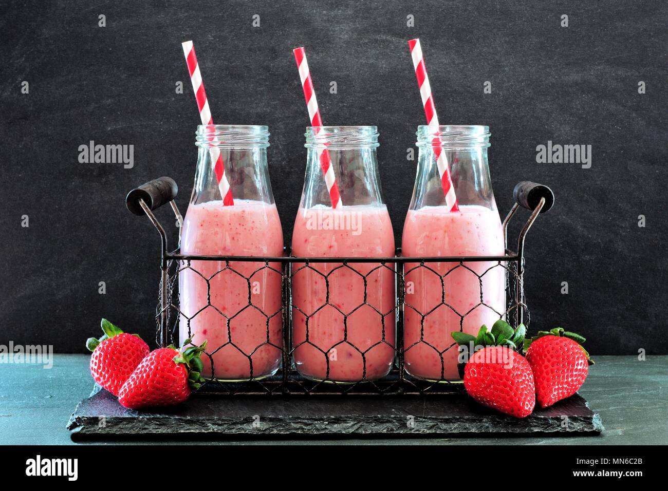 Les smoothies fraises dans des bouteilles avec des pailles dans un panier métallique contre un arrière-plan en ardoise foncé Banque D'Images