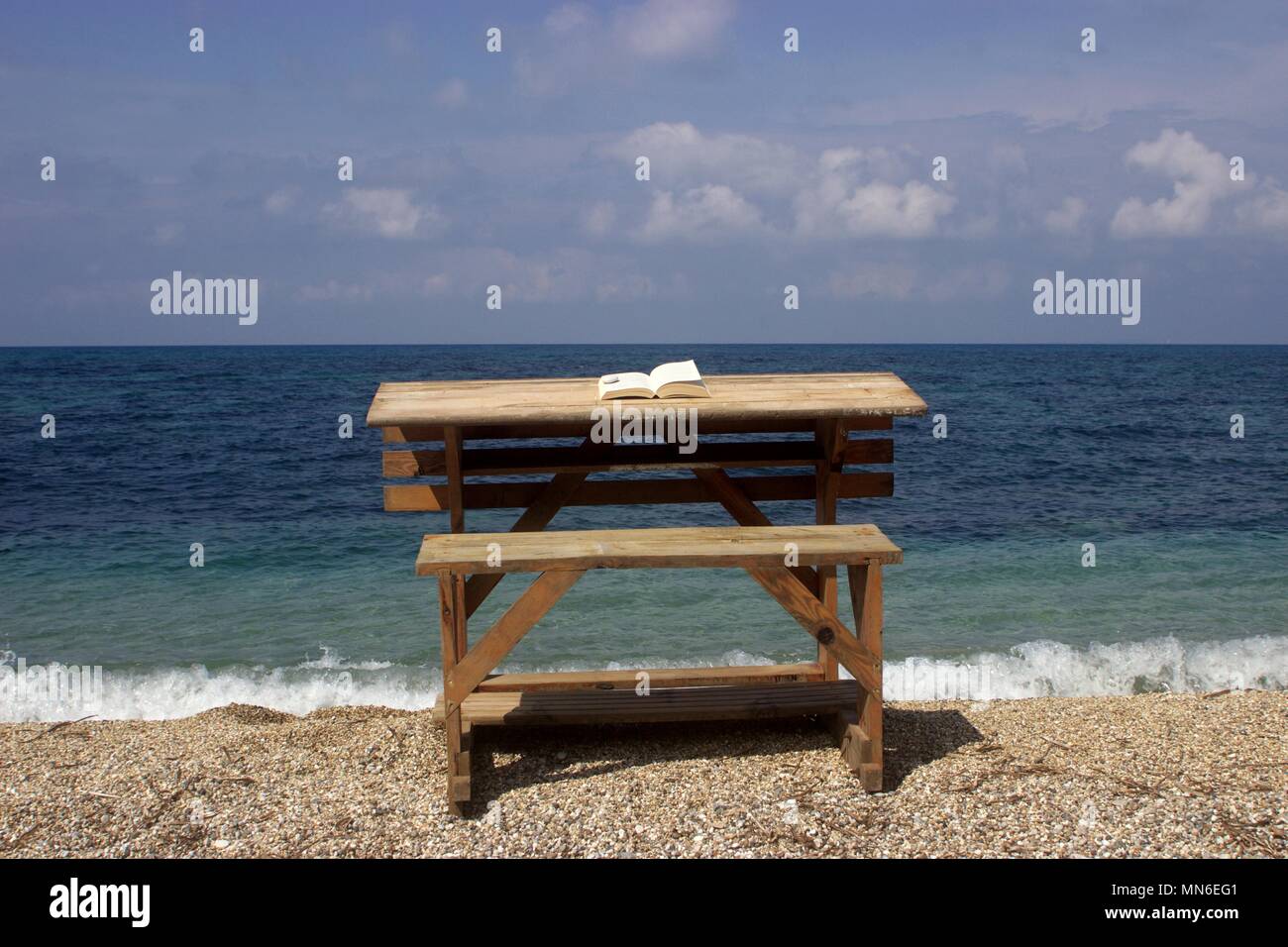 Bureau en bois sur une plage avec un livre ouvert sur elle et d'une mer bleue en arrière-plan Banque D'Images