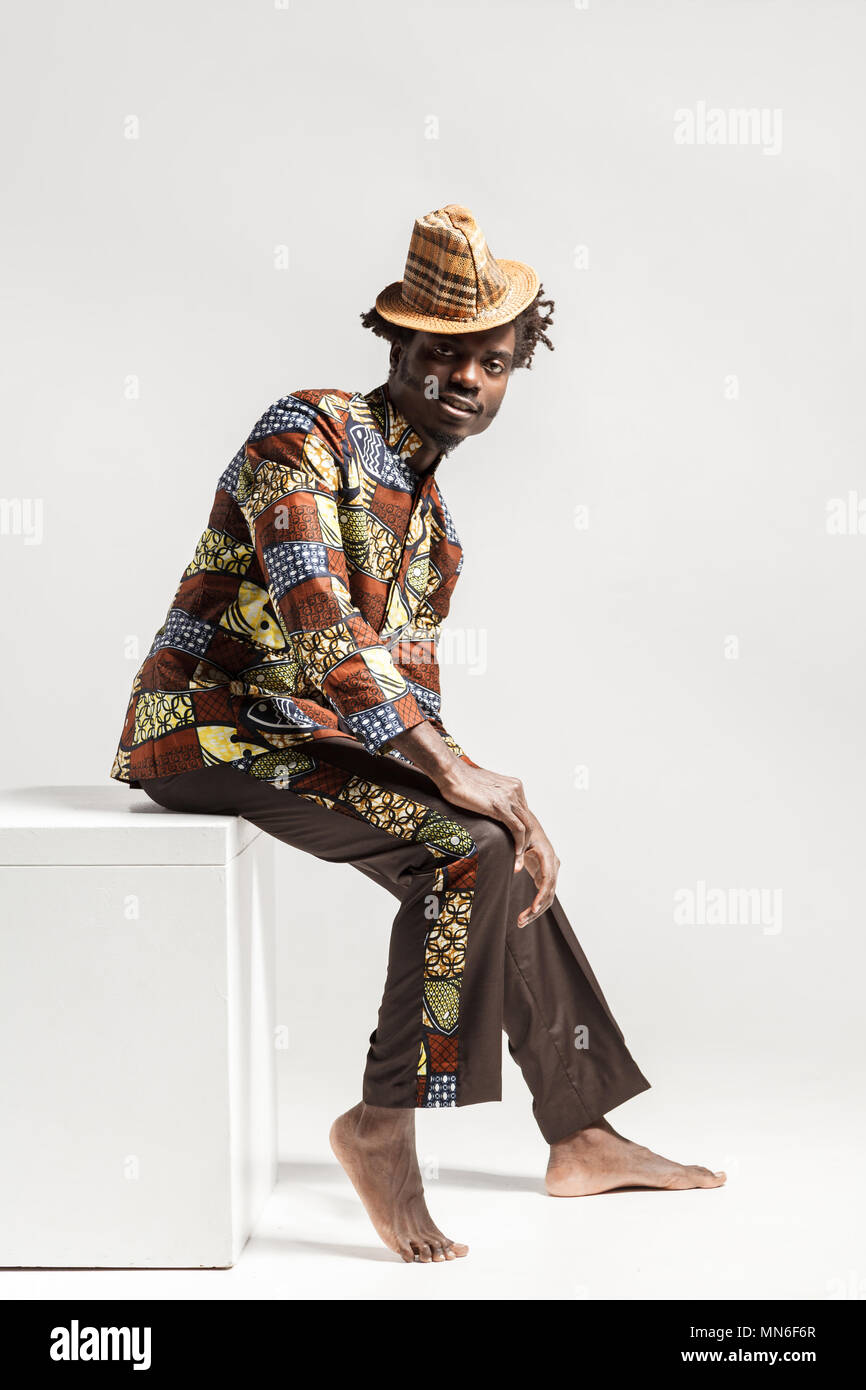 Heureux homme afro de mode en vêtements traditionnels siègent à coub . Piscine, isolé sur fond gris Banque D'Images