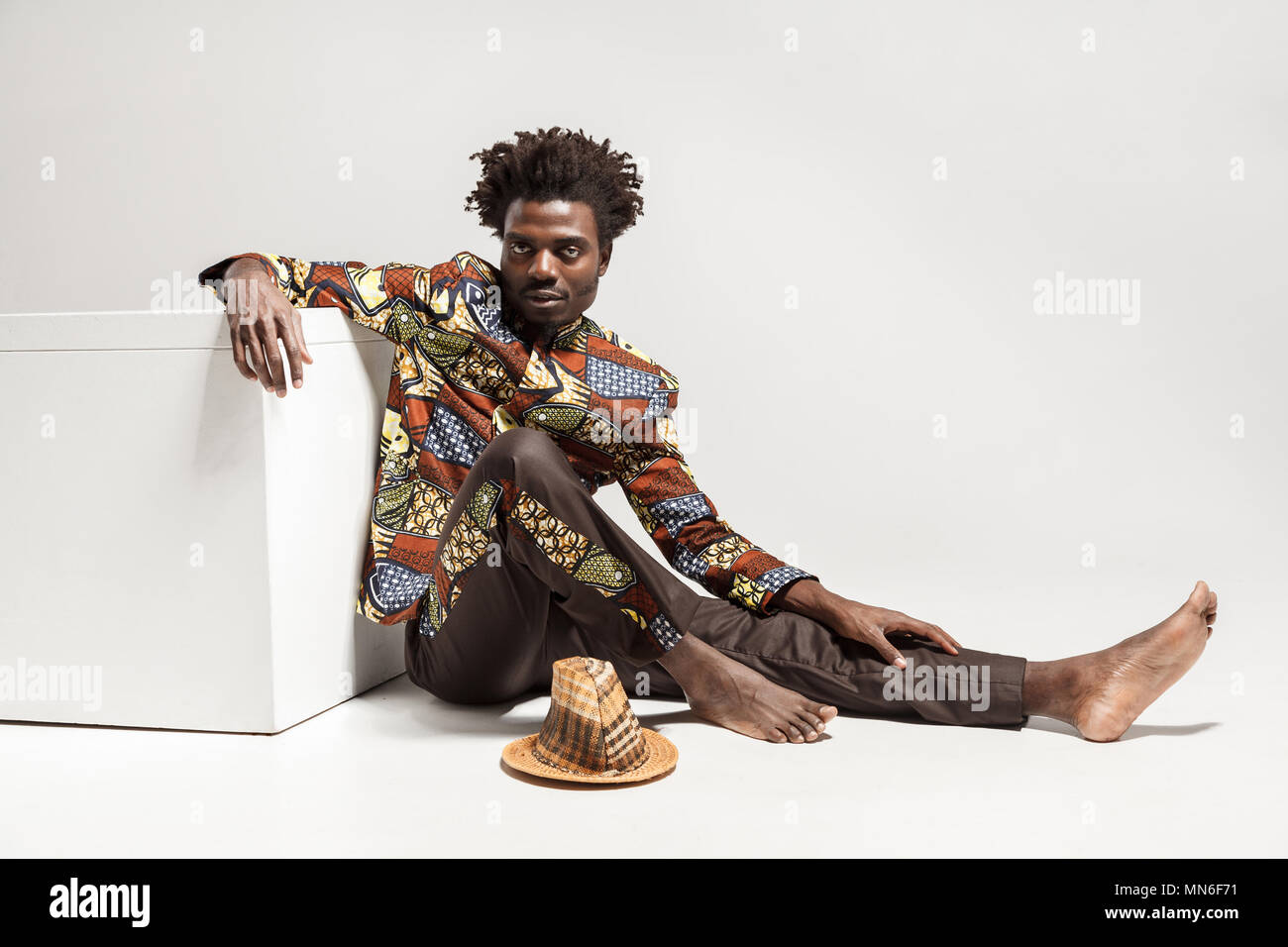 Jeune adulte homme africain, assis sur le plancher près de coub. Piscine, isolé sur fond gris Banque D'Images