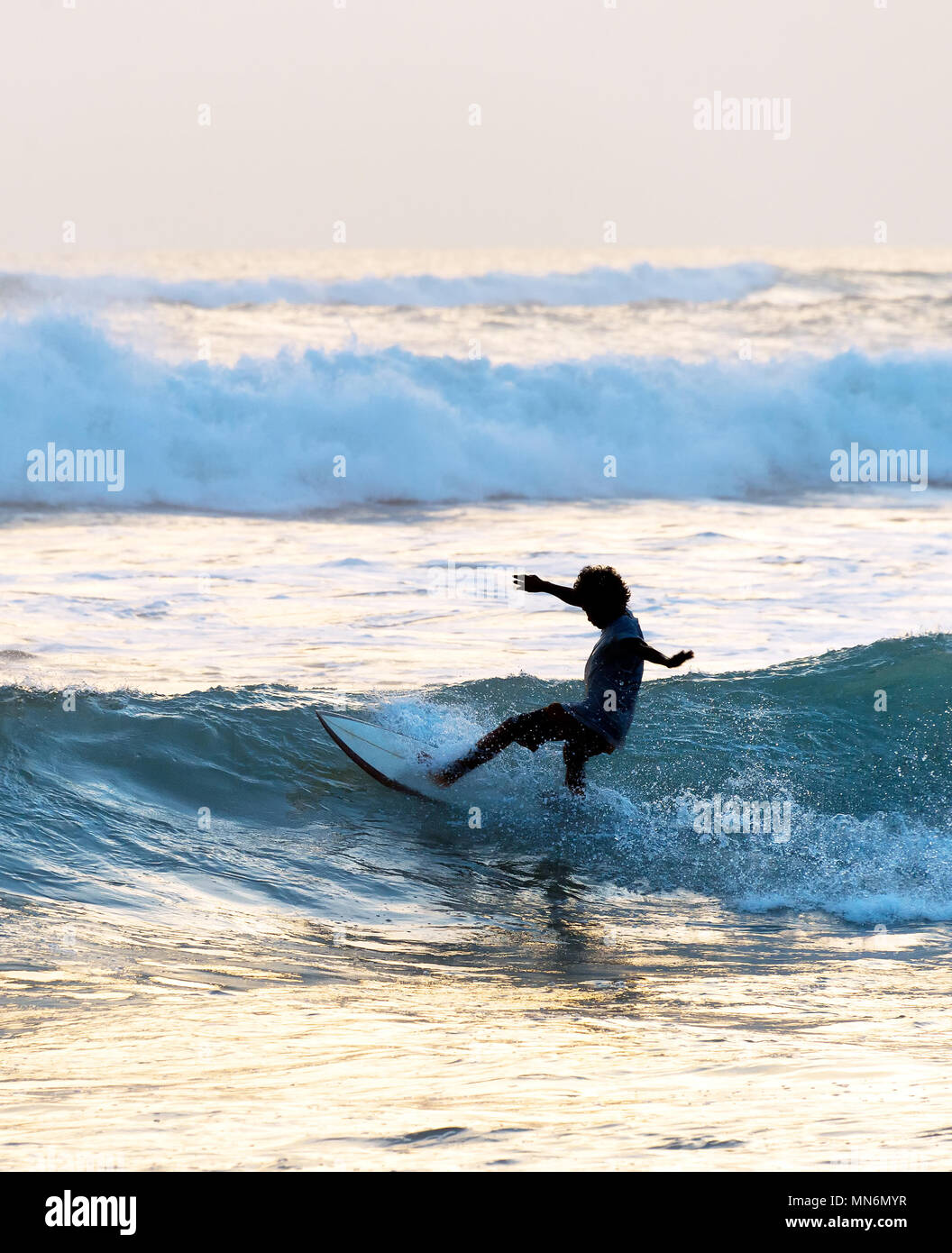 Surf surfer dans l'océan au coucher du soleil. L'île de Bali, Indonésie Banque D'Images