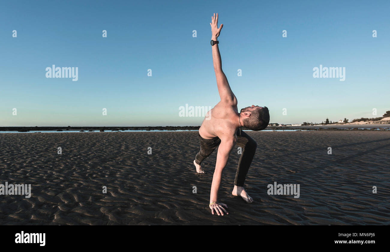 Jeune homme faisant du yoga sur la plage de sable de Sanlucar de Barrameda quand la marée est basse Banque D'Images