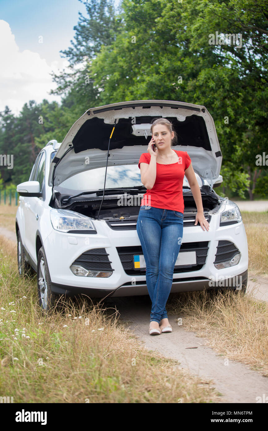 Young woman leaning on casse voiture en terrain et parler par téléphone Banque D'Images